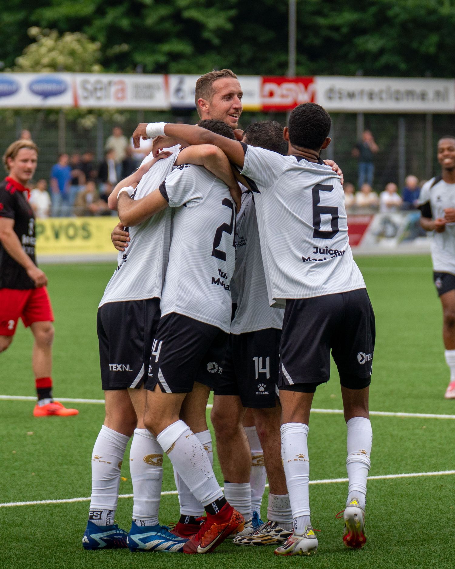 Soccer teammates celebrate together on the field during a match, hugging and embracing in their white uniforms.