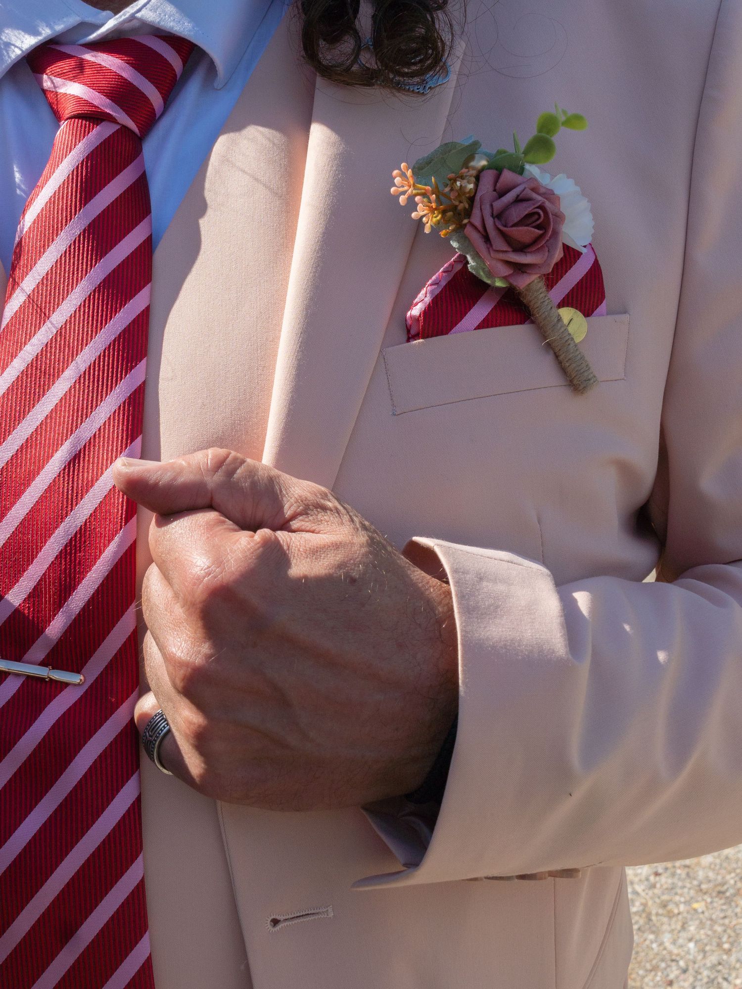 A close-up sequence showing hands adjusting a red and white striped tie and boutonniere against a light-colored suit.
