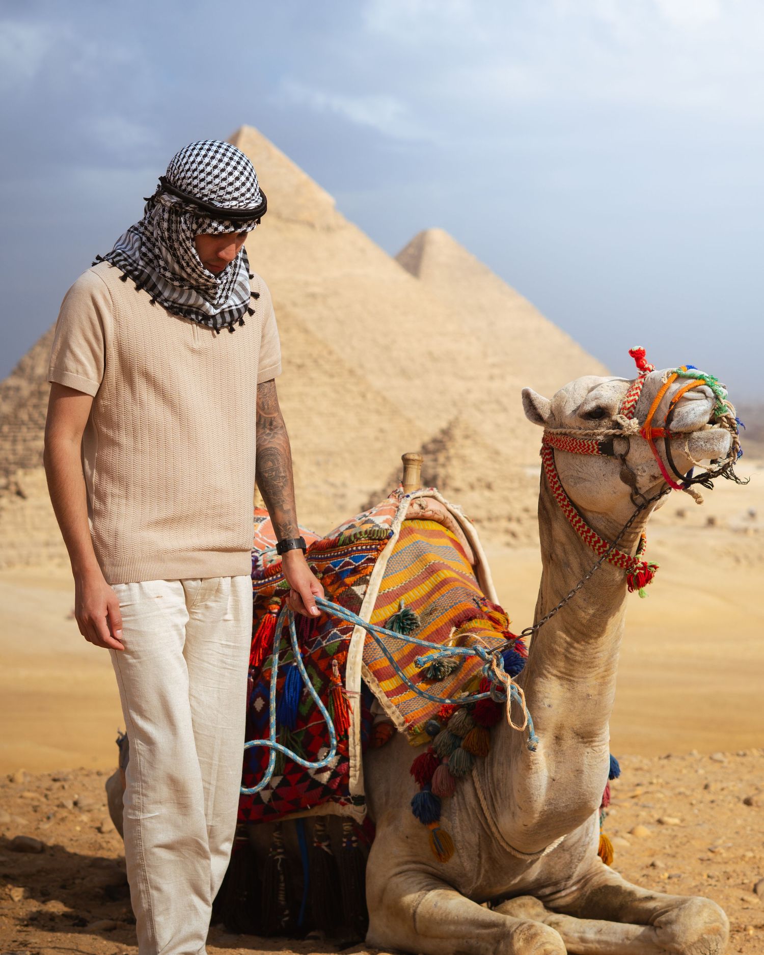 Tourist rides decorated camel near ancient Egyptian pyramids in Giza desert against golden sand and blue sky backdrop.