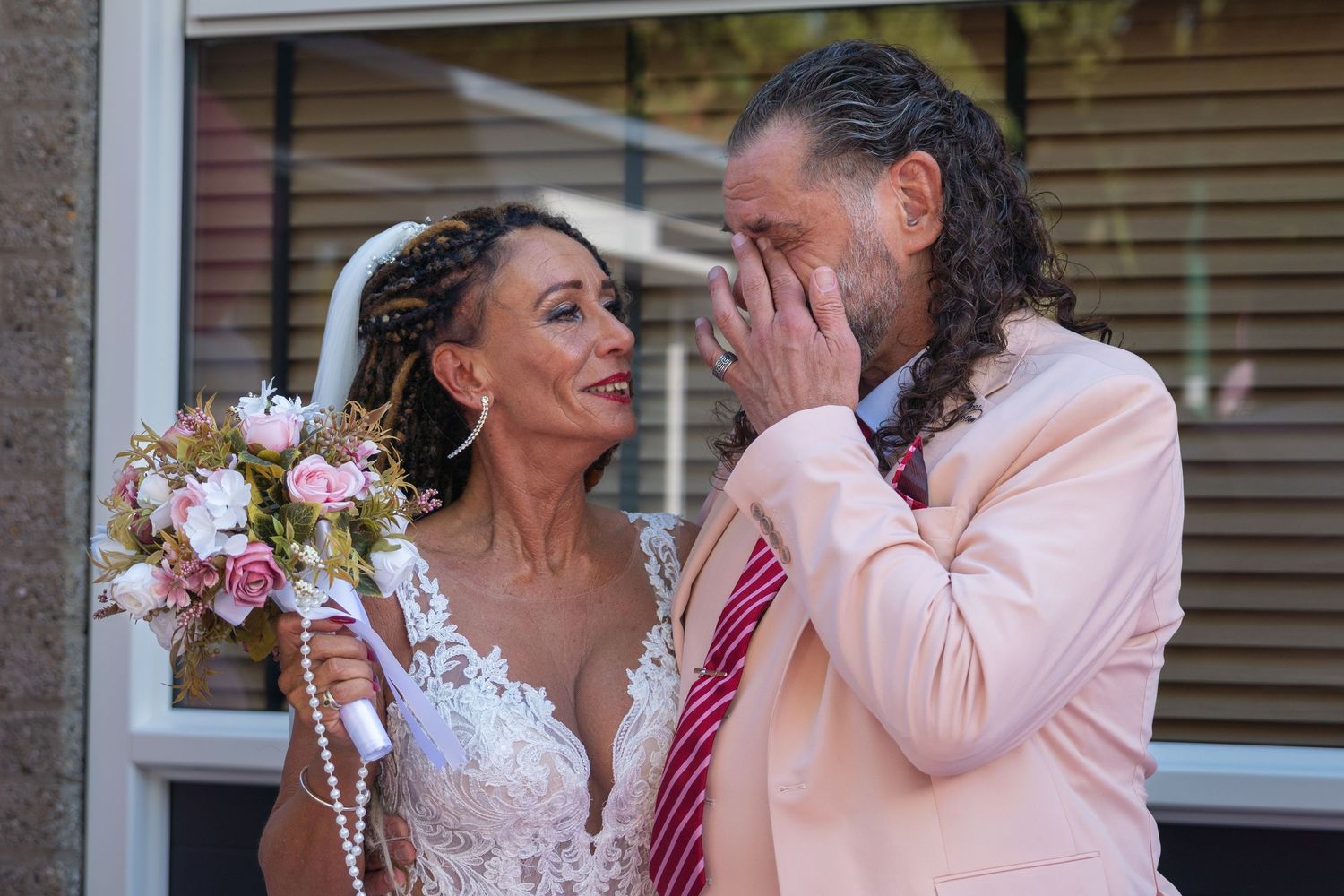 A couple shares a tender moment during their wedding celebration with pink floral bouquet and formal attire.