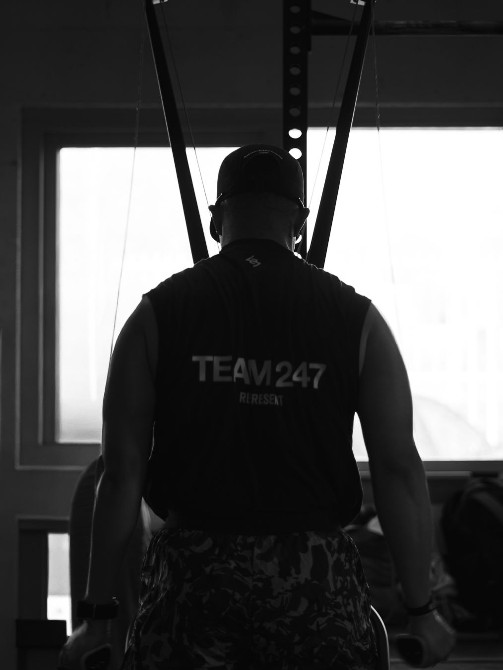 Silhouette of a person wearing a Team247 vest shown from behind in dramatic black and white lighting.