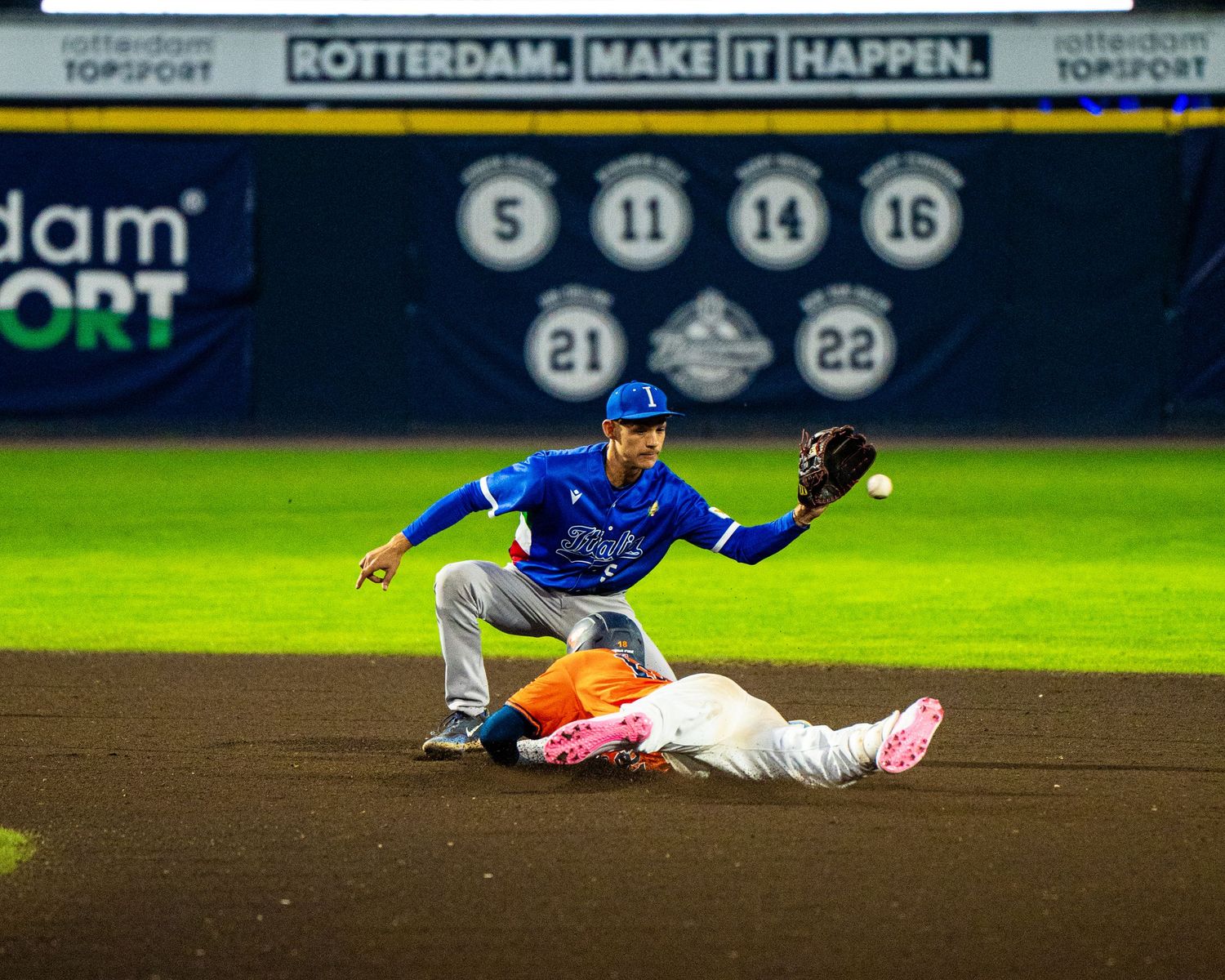 Baseball players in action during night game with sliding play at second base.