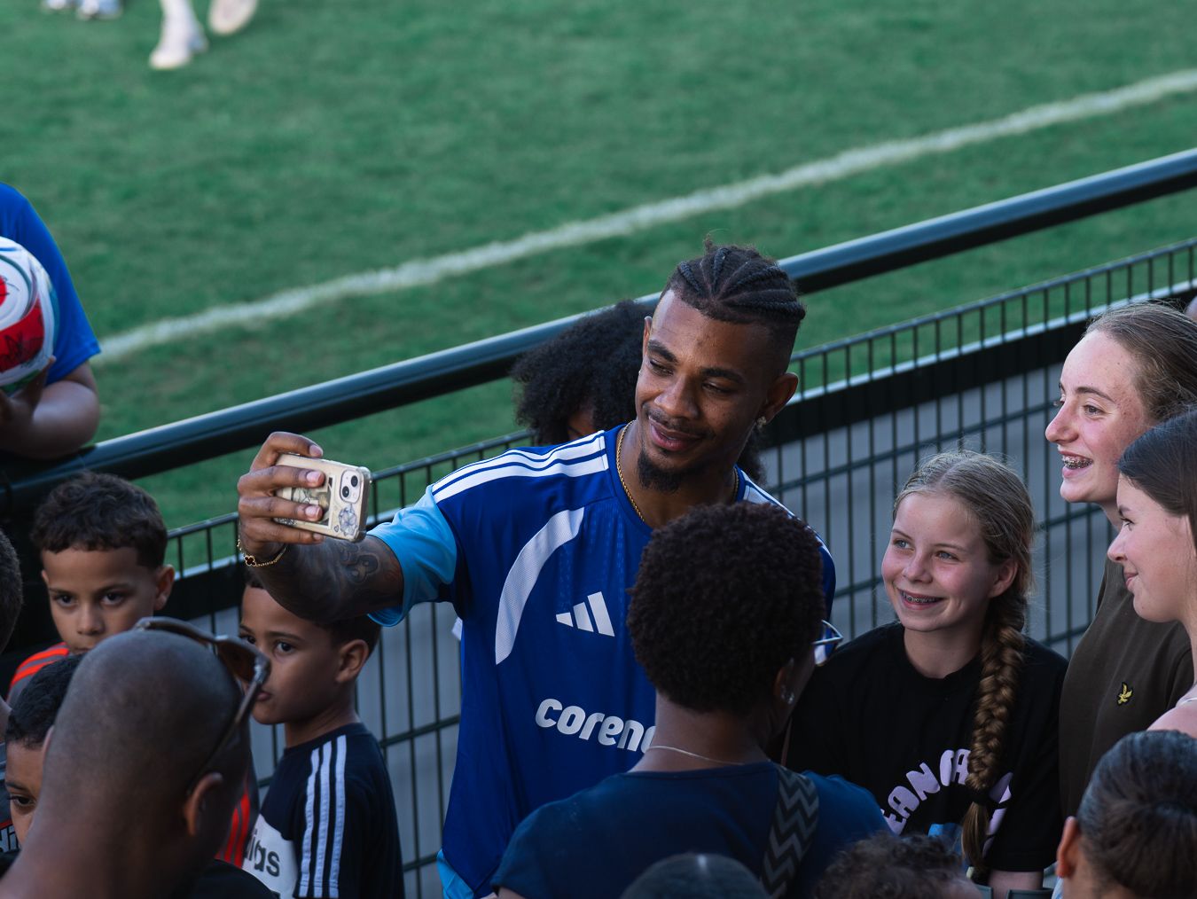 Soccer player in blue jersey takes selfie with smiling fans at stadium during meet and greet event.