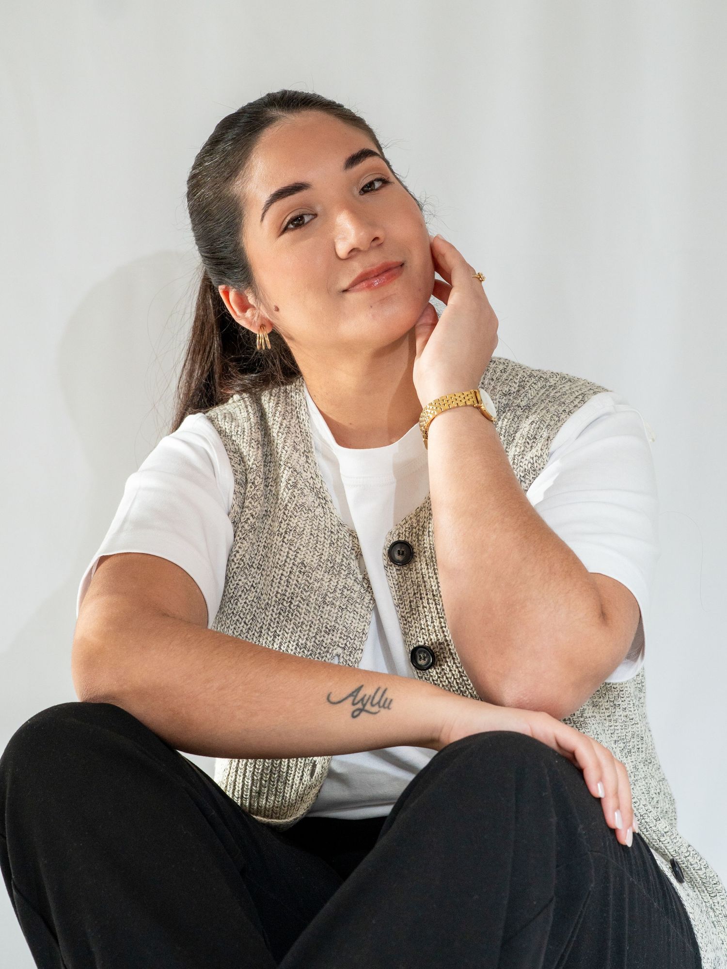 A person in a white top and black pants sits in a contemplative pose against a light background.