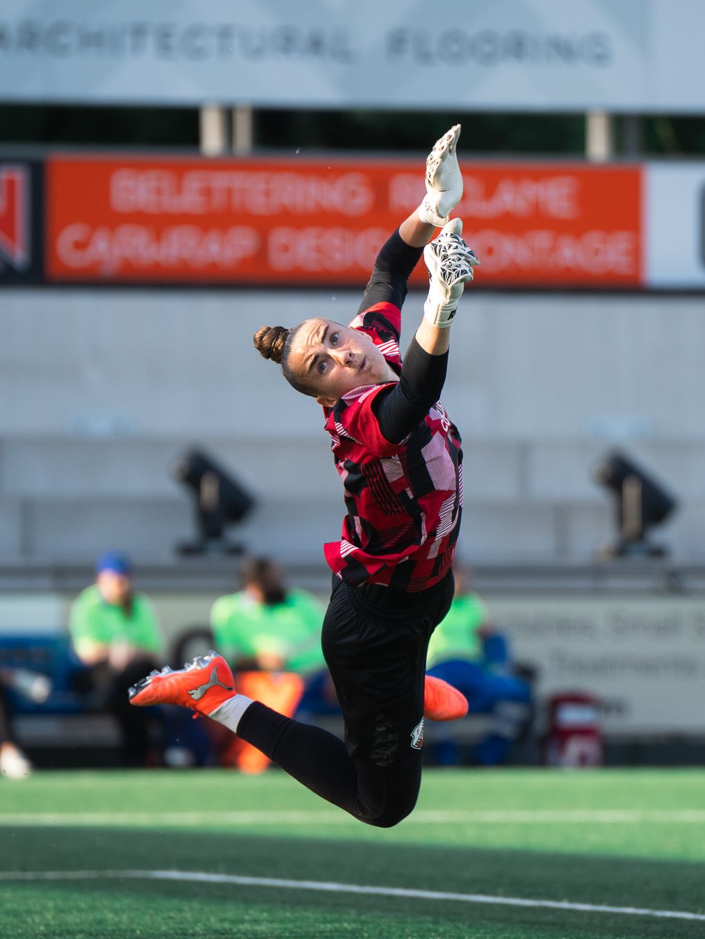 Athlete in black and red uniform leaping mid-air to catch ball during outdoor sports match on green turf field.
