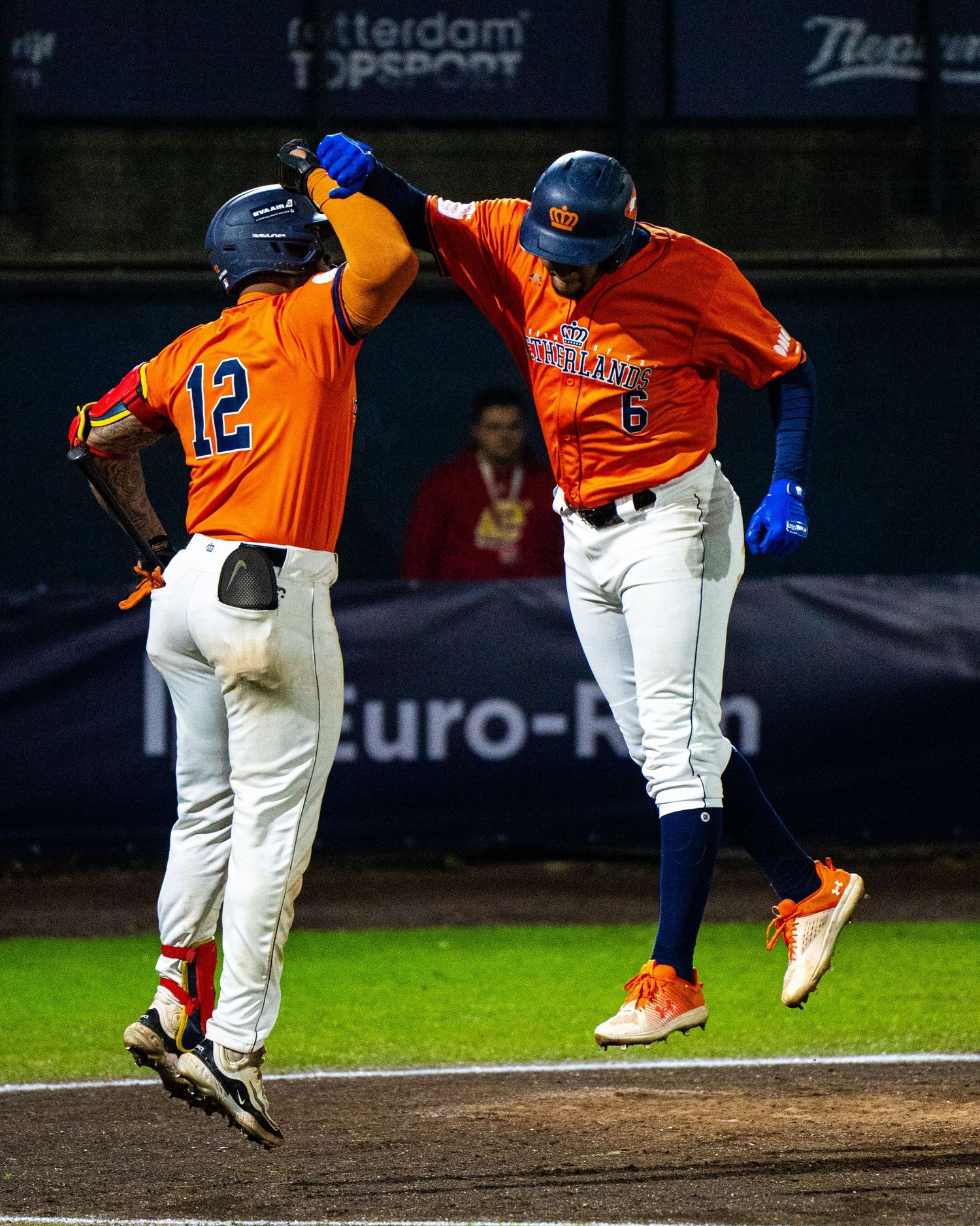 Baseball player in orange jersey slides into base during night game while opponent attempts to make the tag.