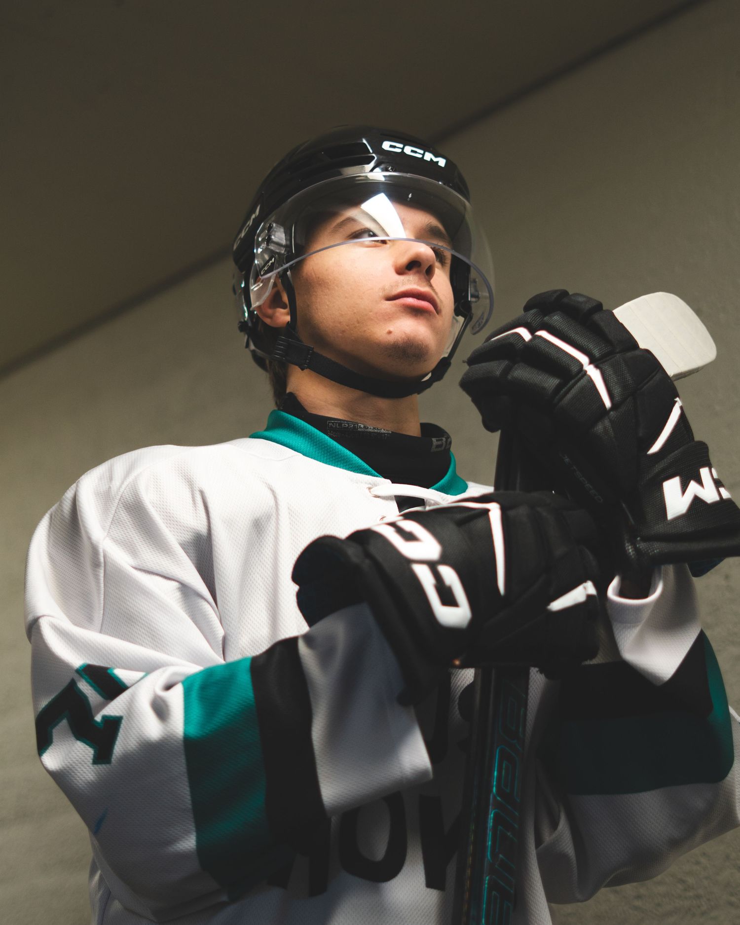 Hockey player in white and teal jersey adjusts protective equipment while looking upward in a series of action shots.