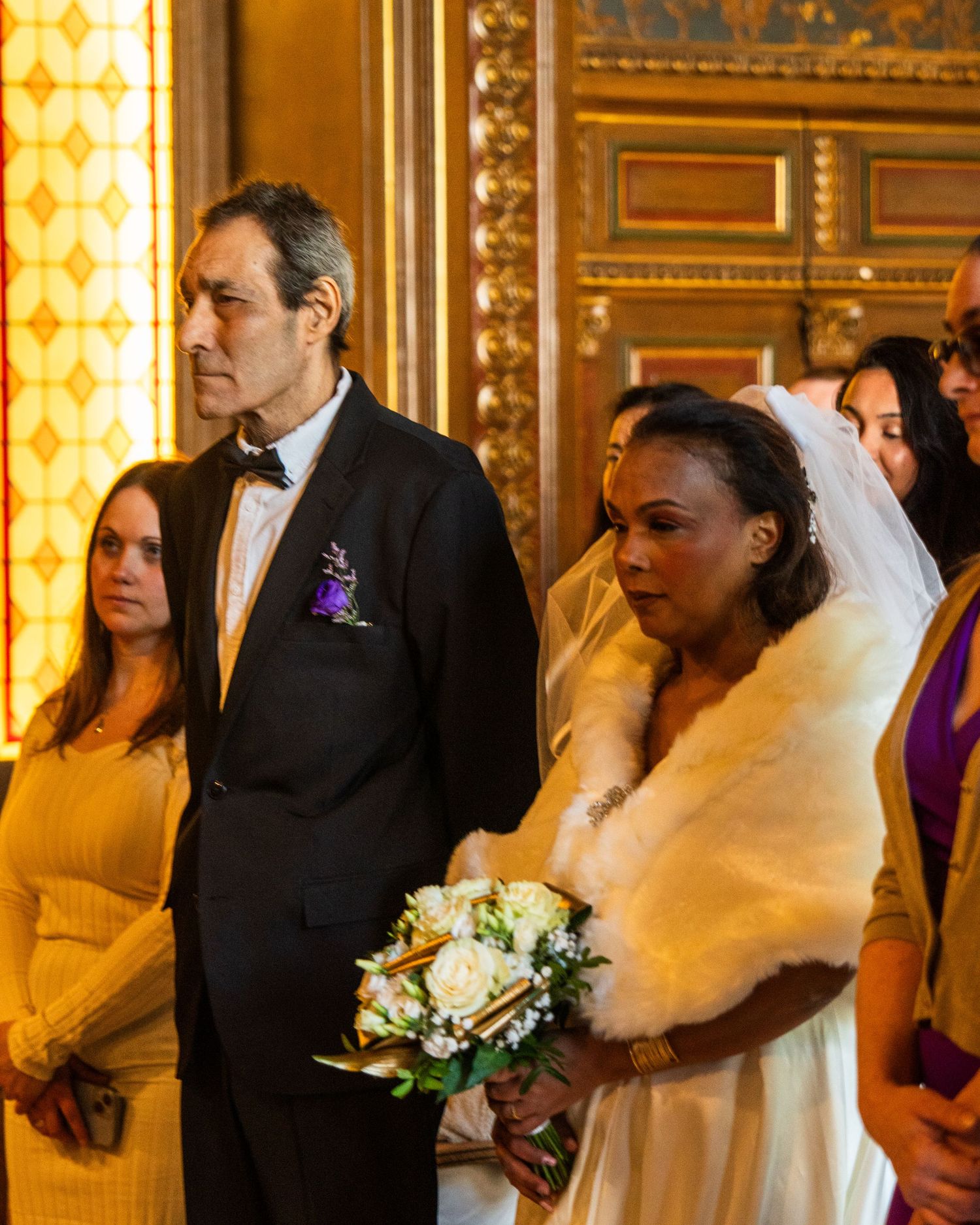Wedding ceremony in ornate gold room with bride in white dress and fur stole.