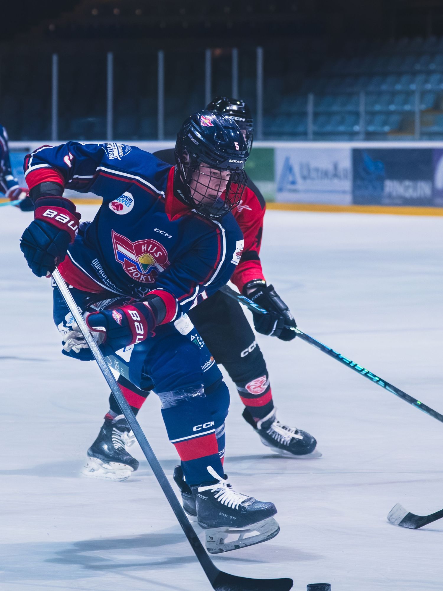 Hockey player in navy and red uniform glides across ice while controlling puck during competitive match.