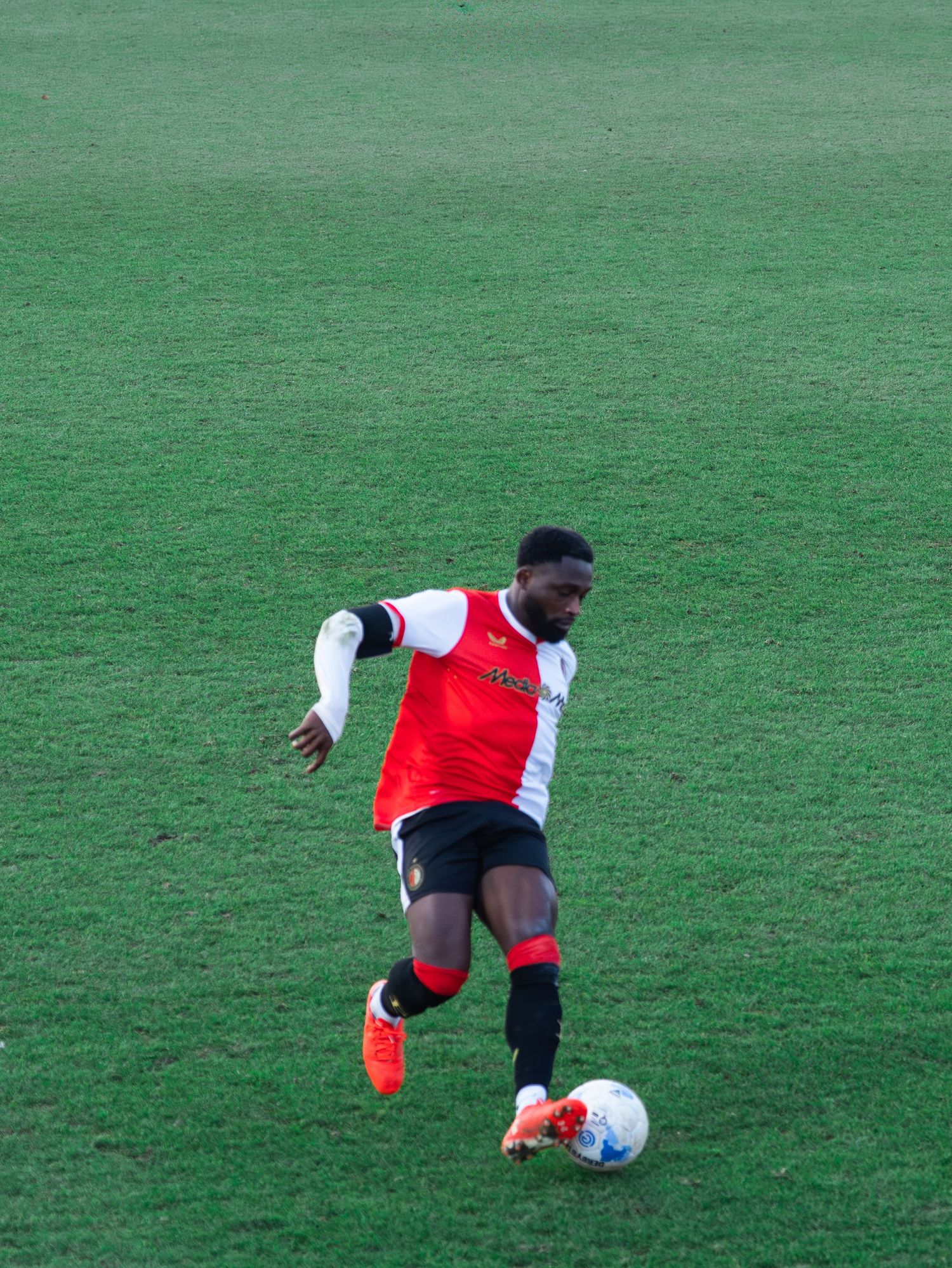 Soccer player in red and white jersey dribbles ball on green grass field during match.