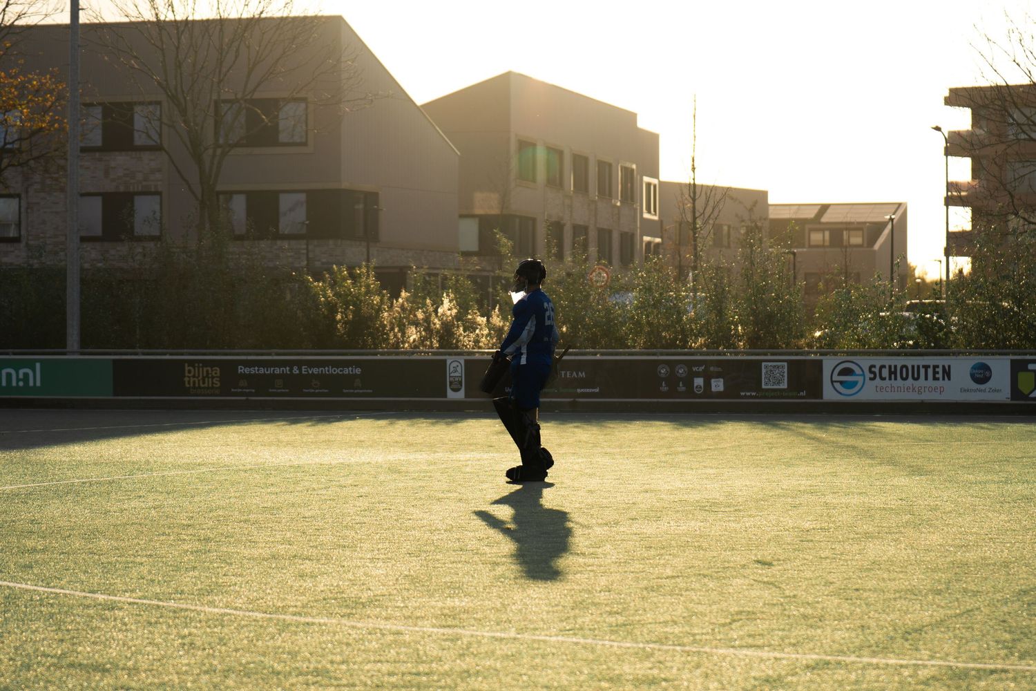 A silhouette plays tennis on a court at sunset with apartment buildings in the background.