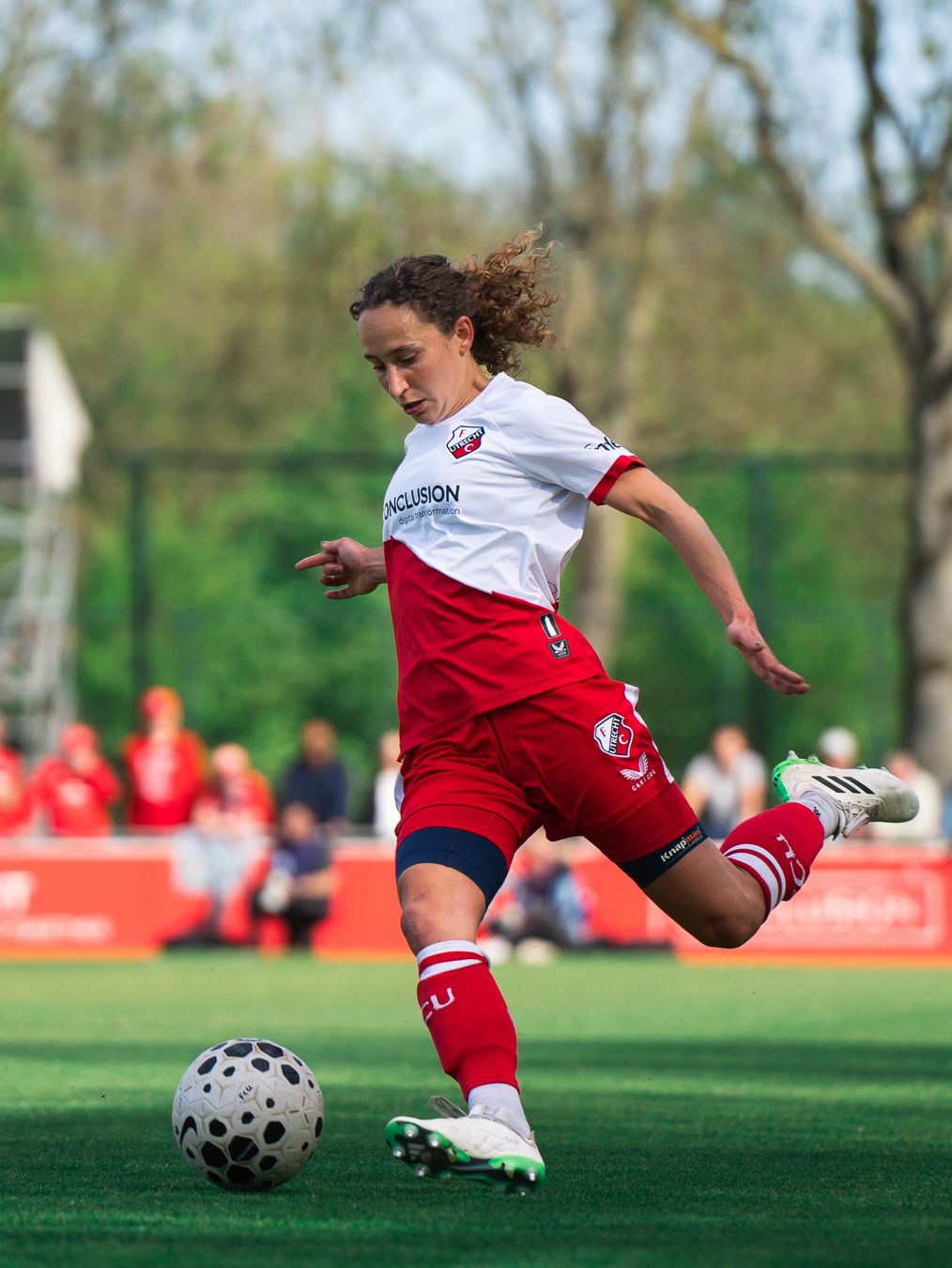 Female soccer player in red and white uniform kicking a ball on an outdoor field.