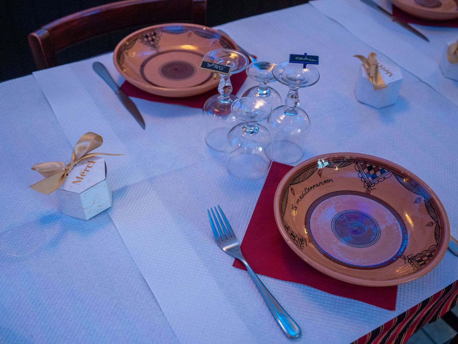 Formal place settings with brown plates, wine glasses, and red napkins on white tablecloth.