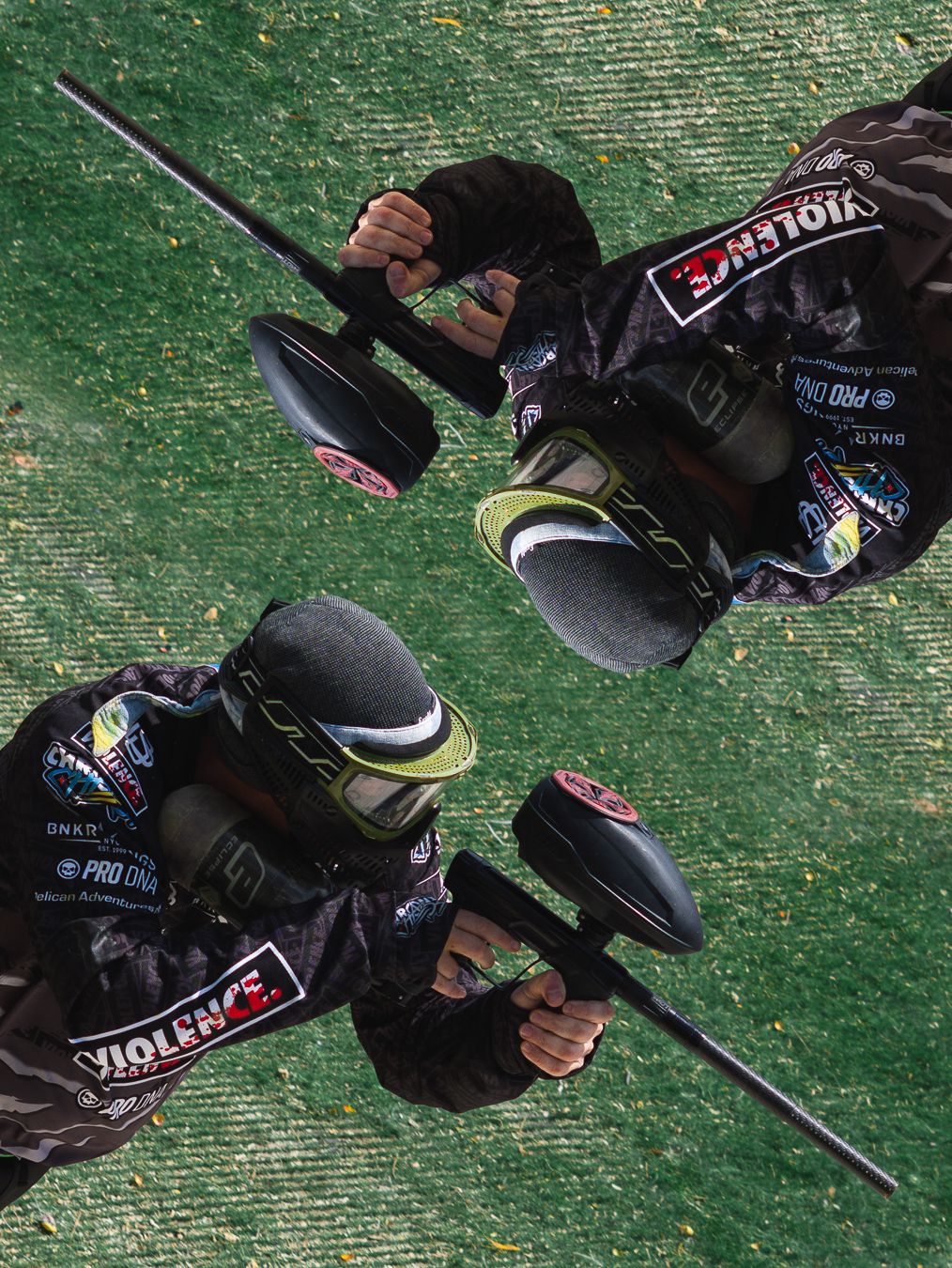 Two paintball players in matching Violence team gear hold markers on a green field, viewed from above.