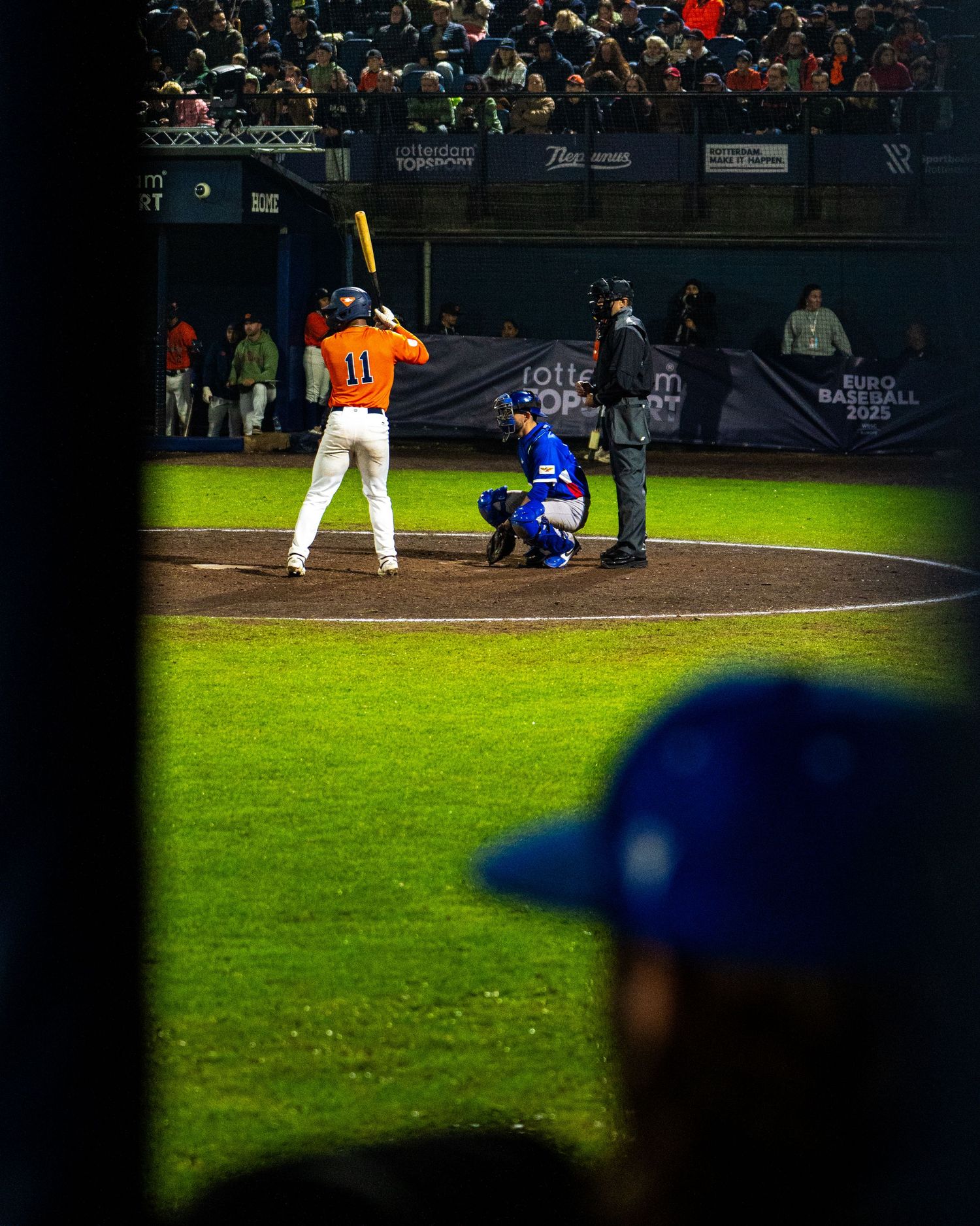 Baseball players on a dimly lit field during a nighttime game with stadium lights illuminating the grass.