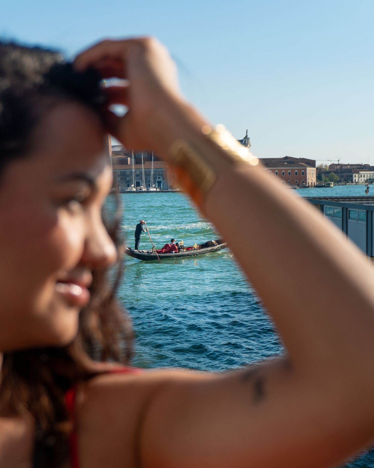 Smiling woman in Venice with a gondolier and historic buildings visible on the canal in the sunny background.
