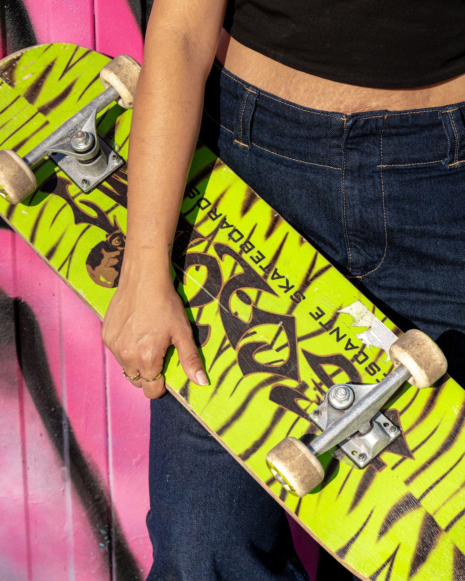 Close-up view of hands holding a neon yellow skateboard against a pink wall background.