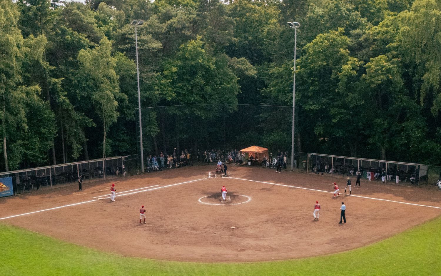 Aerial view of a baseball diamond surrounded by lush green trees with players on the field during a game.