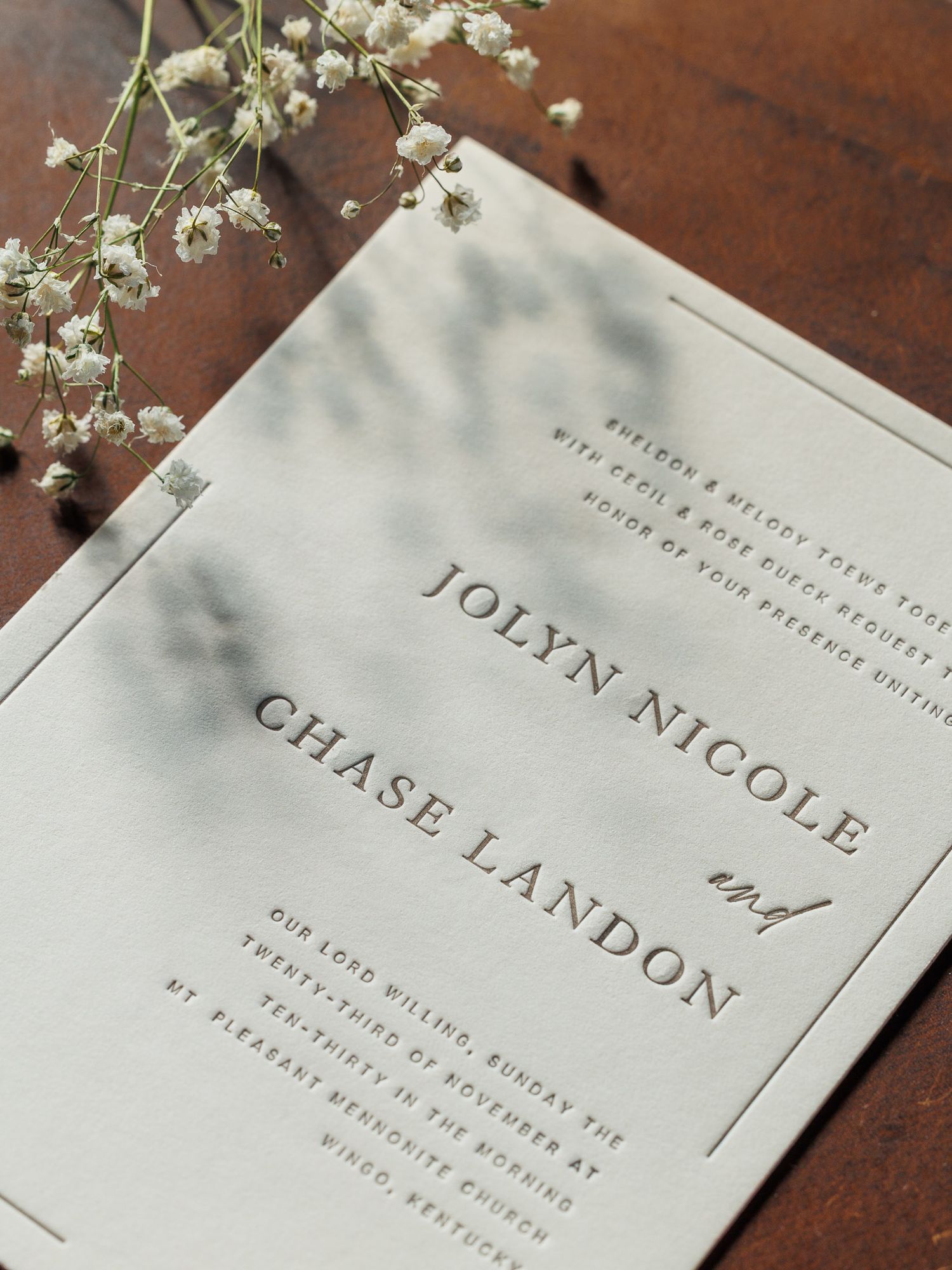 Elegant wedding invitation cards with delicate floral details and minimalist typography on a dark wooden surface.