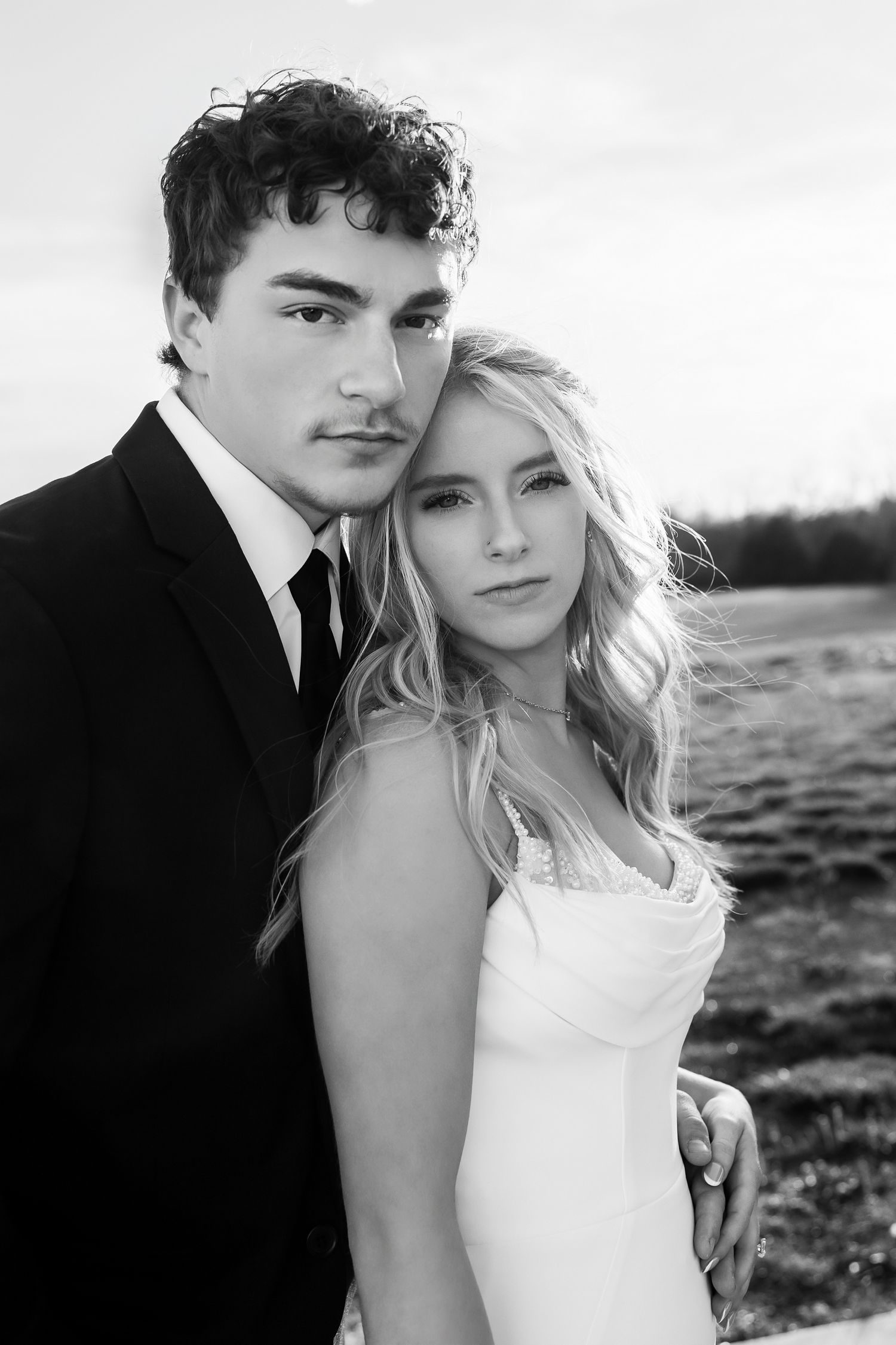 Black and white portrait of a young couple in wedding attire, groom in suit and bride in white dress, outdoors.