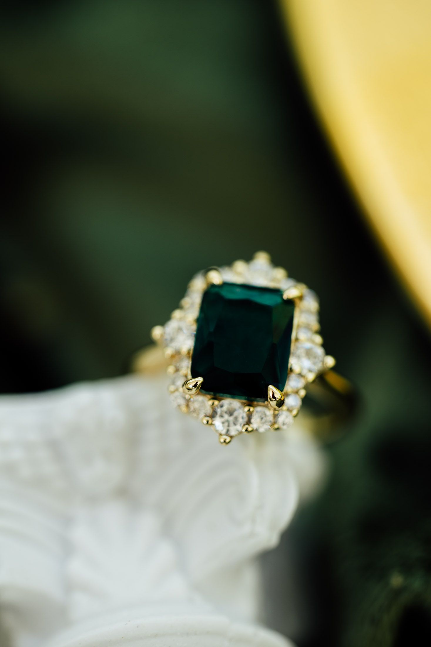Stunning emerald cut green gemstone engagement ring with diamond halo set in gold on white decorative surface.