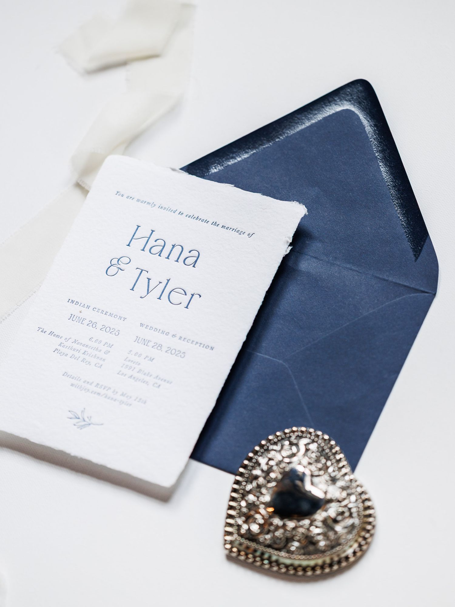 White business cards with navy blue envelopes and a decorative silver brooch displayed in a minimalist arrangement.