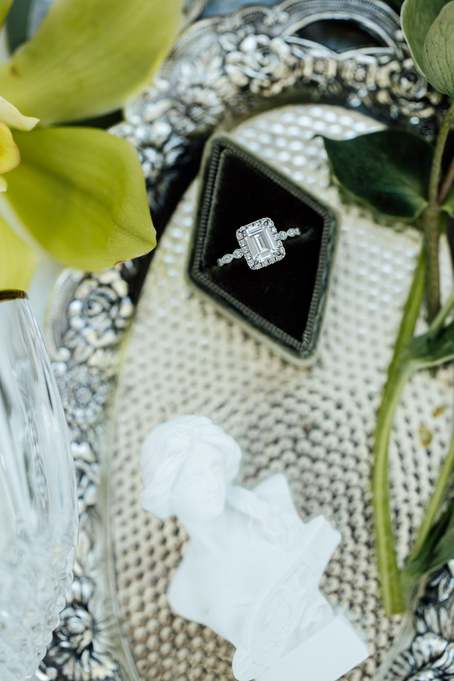 Elegant emerald-cut diamond halo engagement ring displayed in a black velvet box on a decorative silver tray.