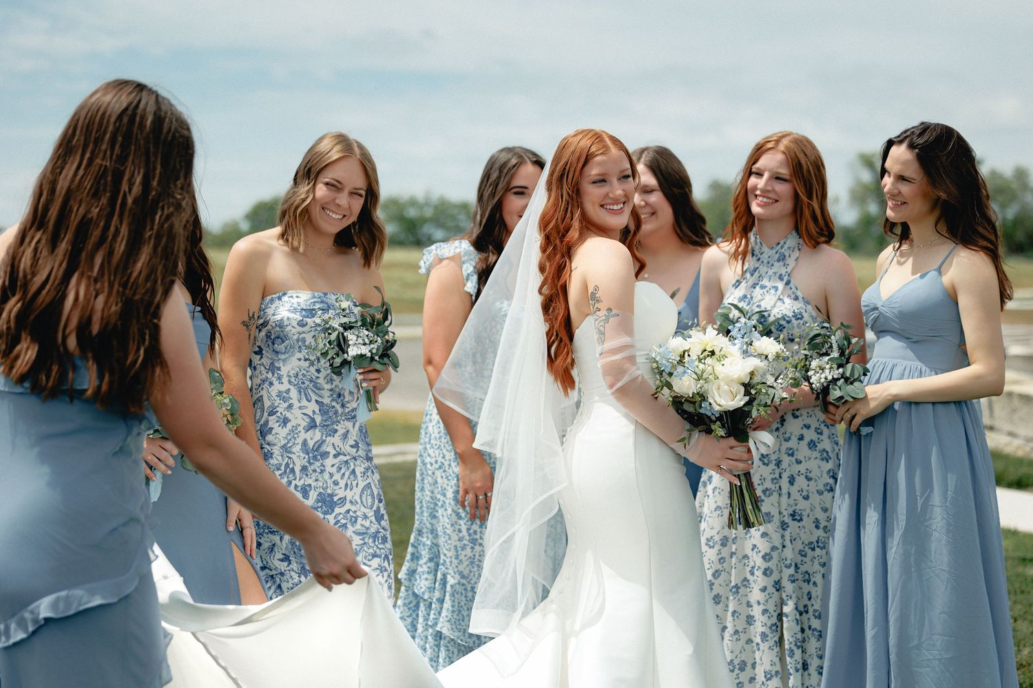 Bridesmaids in light blue dresses gather around bride in white gown outdoors during a Wichita Wedding Photography session