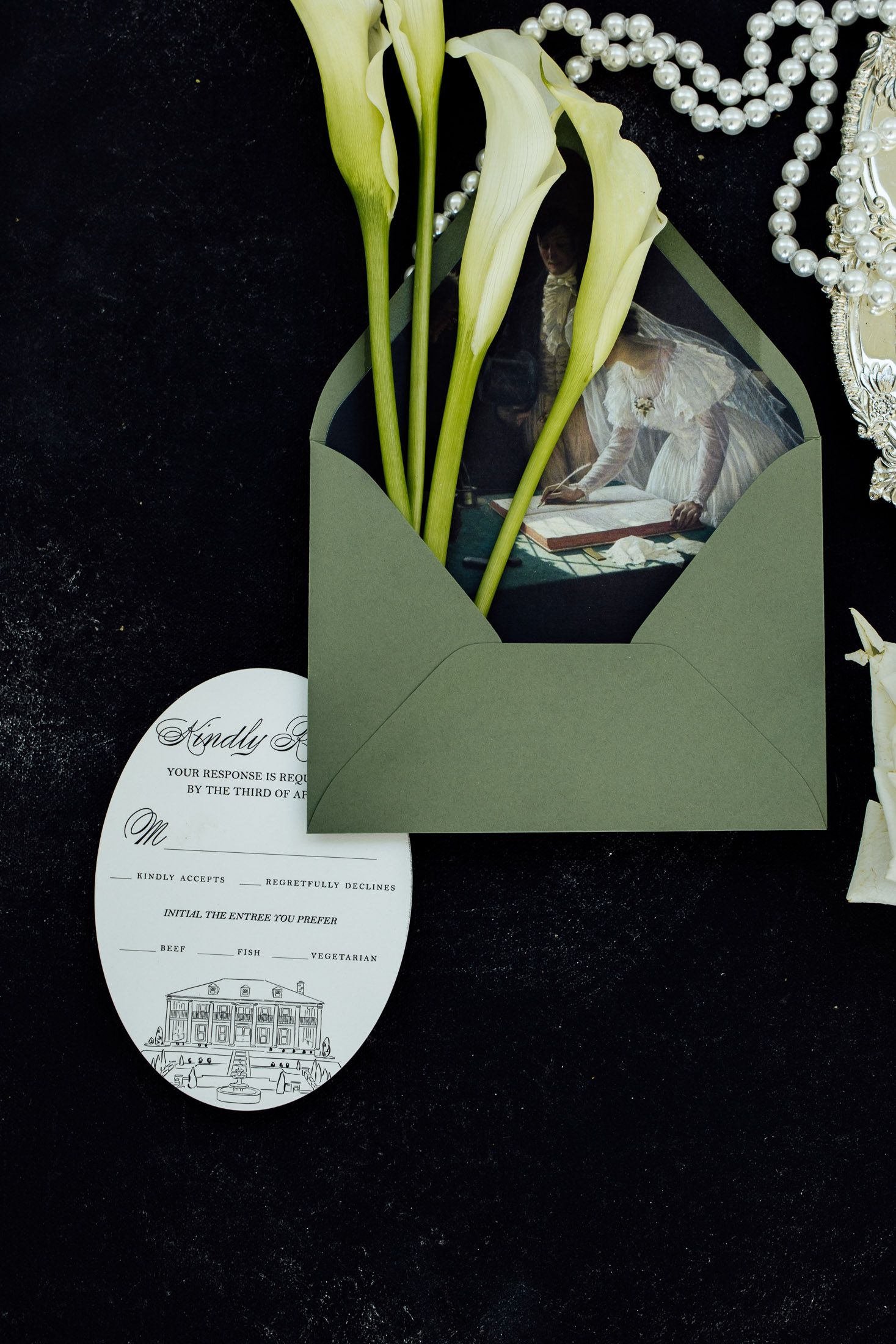 Elegant wedding invitation suite with green envelope, calla lilies, pearl necklace, and oval RSVP card on dark background.