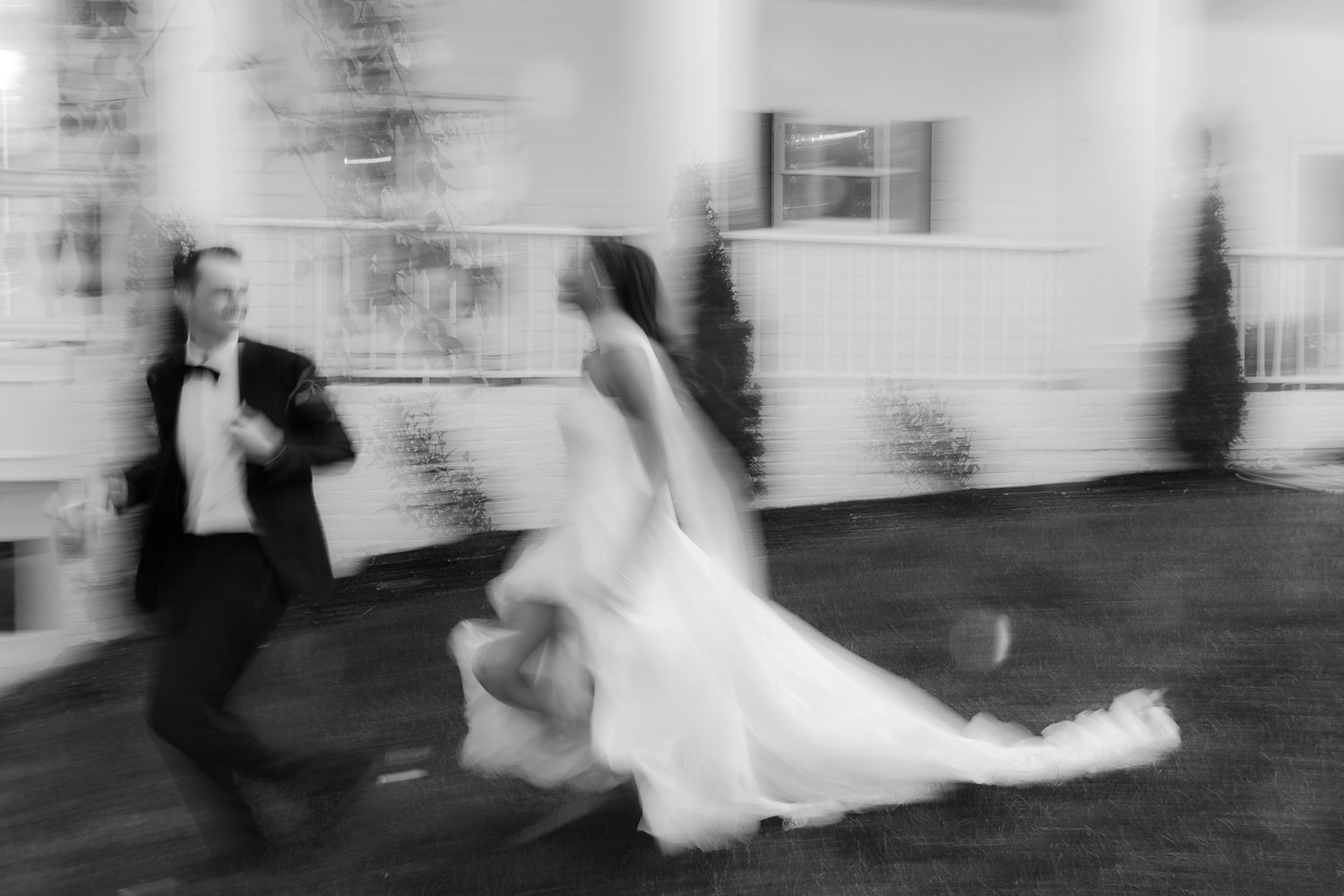 Blurred black and white photo of bride and groom dancing joyfully at their wedding reception outdoors.