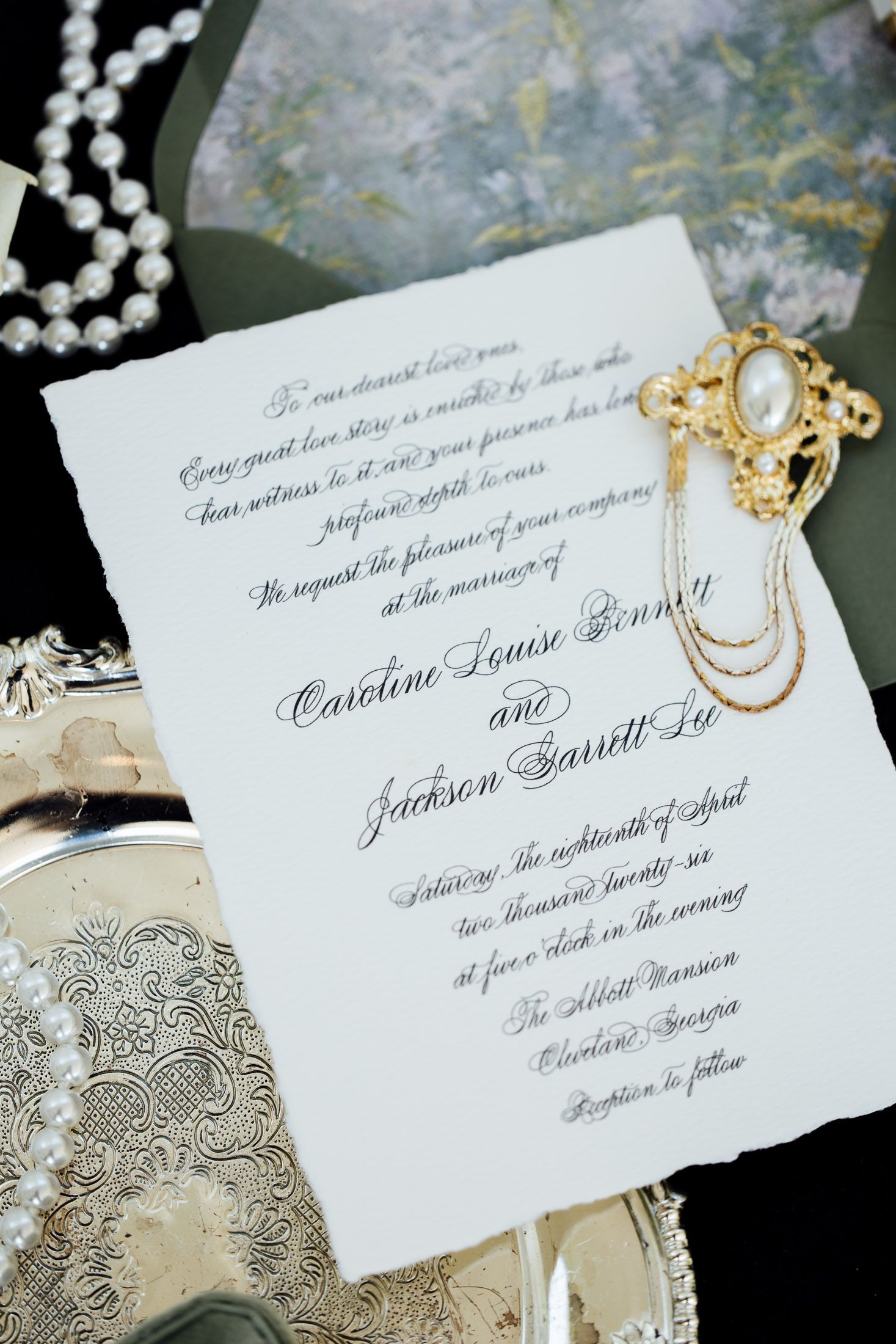 Elegant wedding invitation for Caroline Louise Ginny and Jackson Garrett Lu, displayed with pearl necklace and gold brooch.