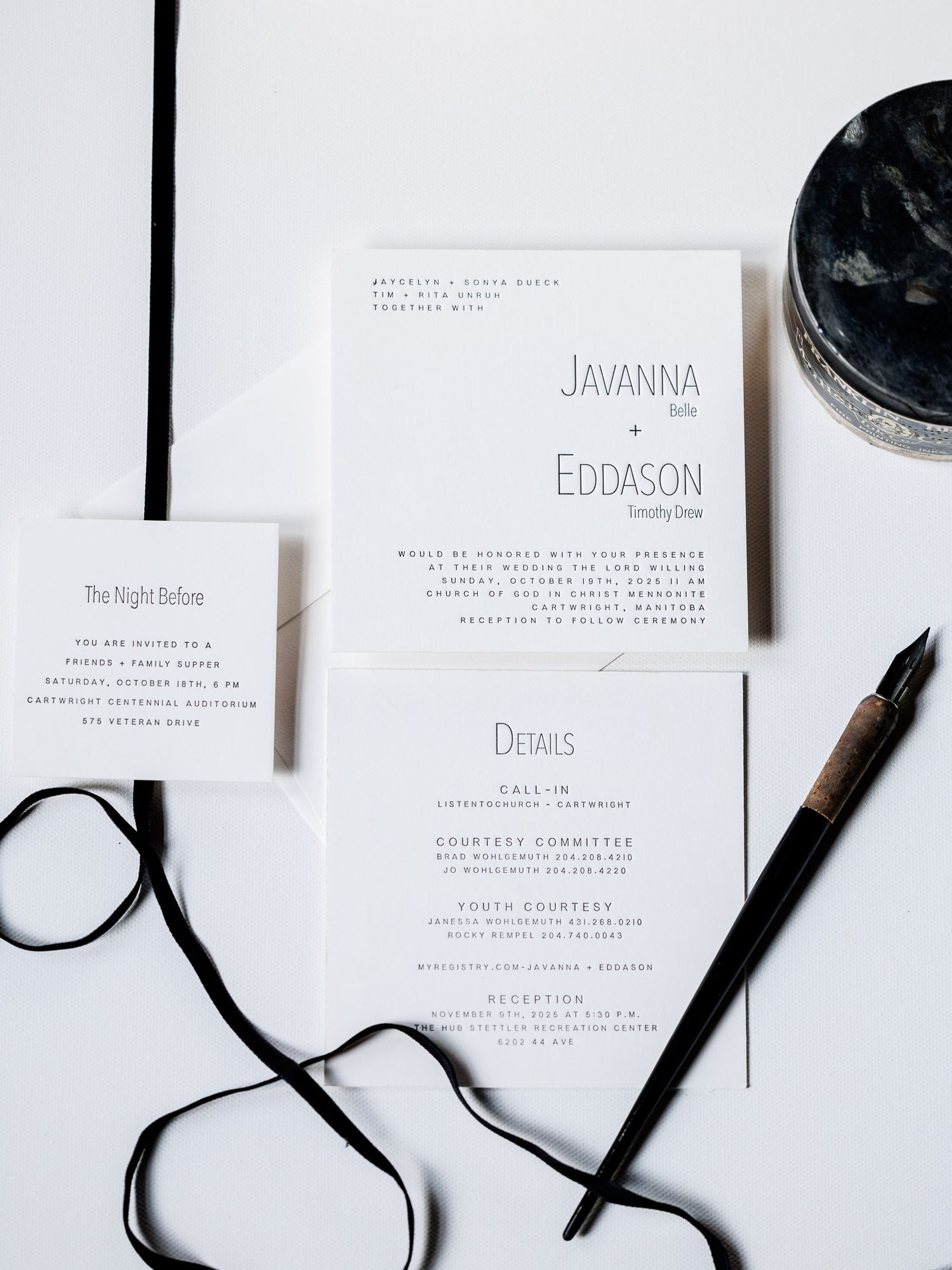 Minimalist wedding invitation suite in white with black calligraphy and ribbon details laid out on white surface.