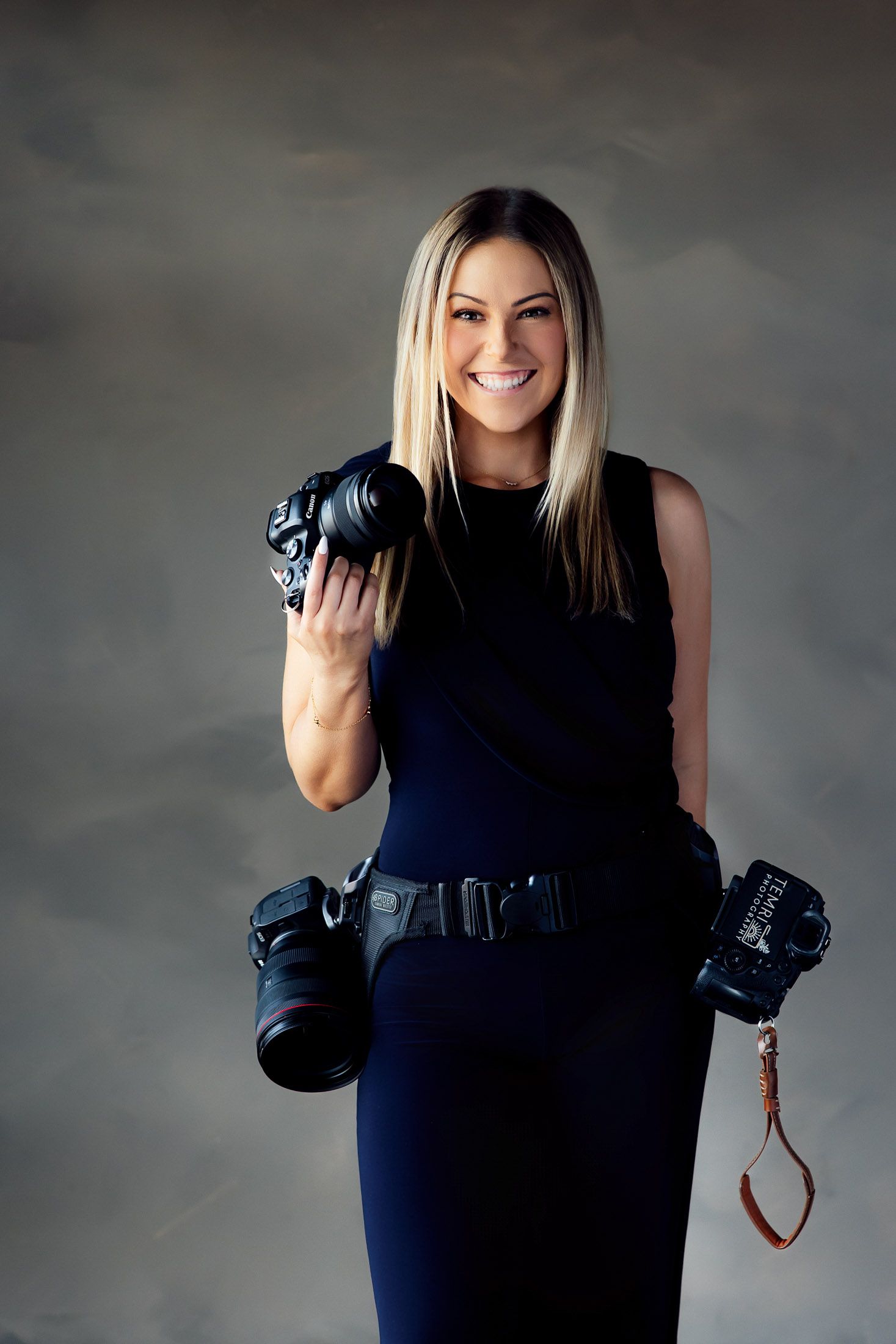 Studio shot of Wichita Kansas wedding photographer carrying camera equipment and professional posing.