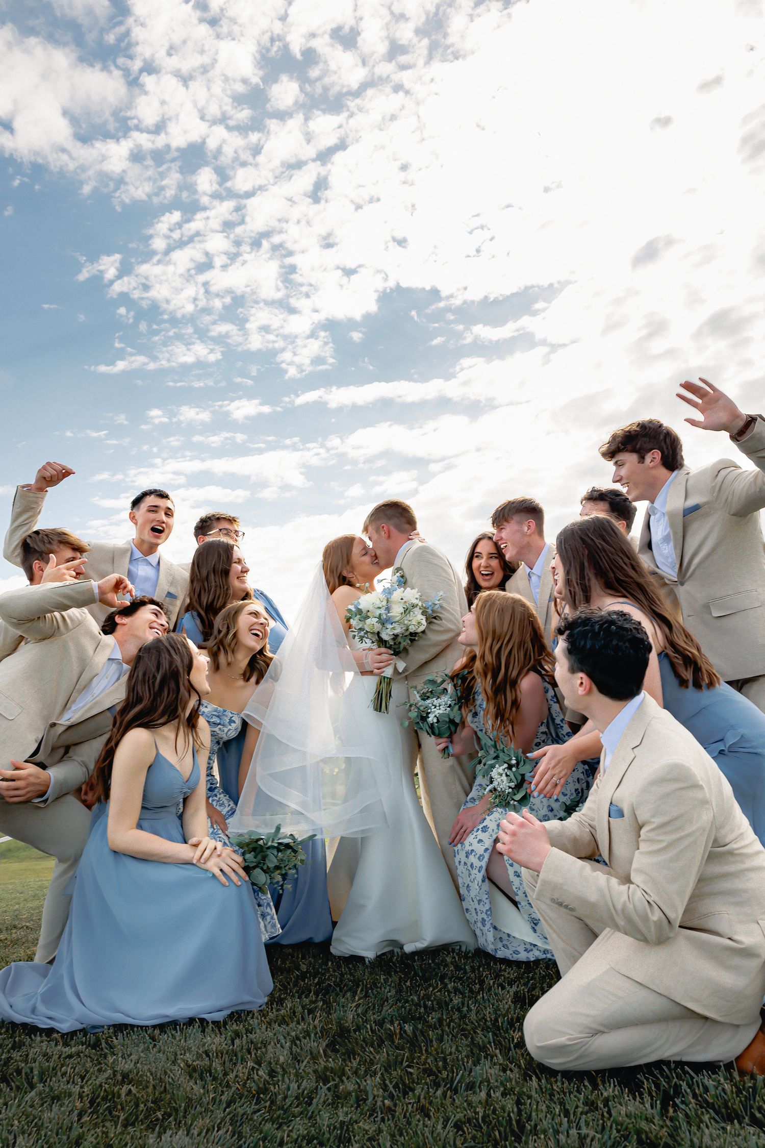 Wichita Wedding party celebrates joyfully on grassy hill with blue sky and clouds in background captured by Temri Photography