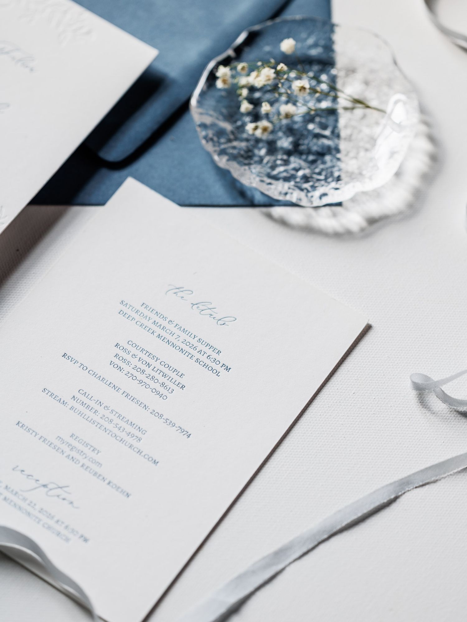 Elegant wedding invitations in white and blue with silver decor elements arranged on a light surface.