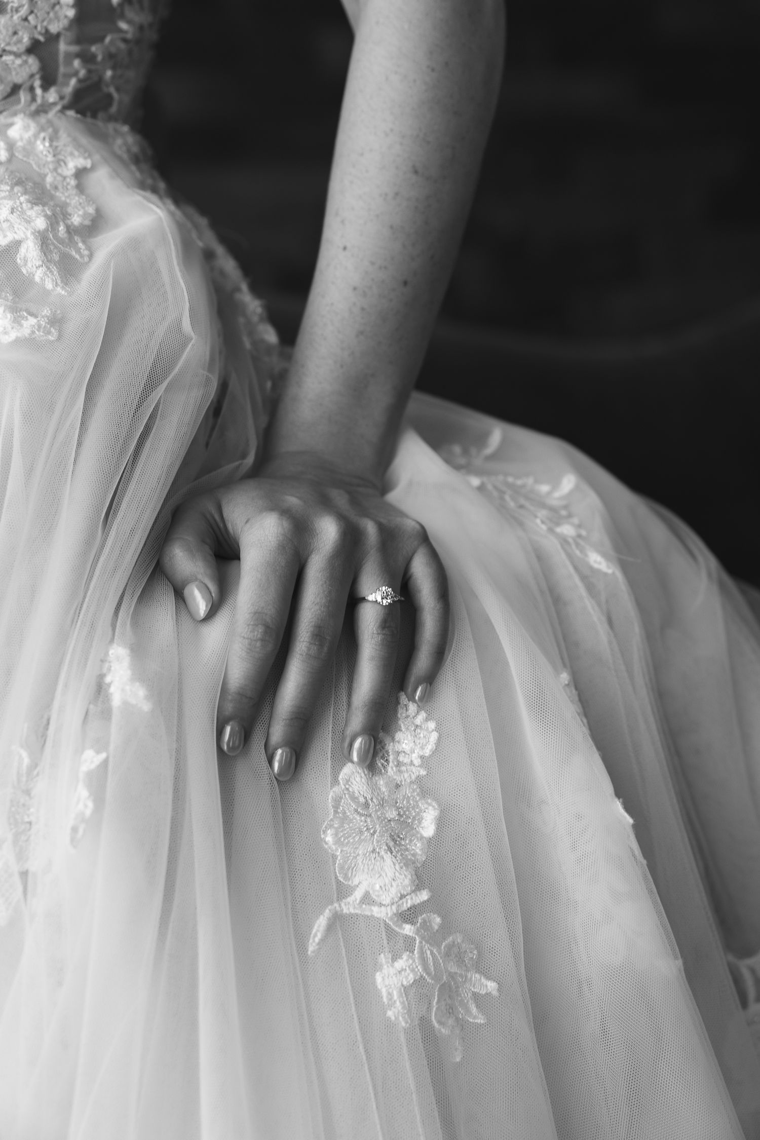 Detail shot of bridal hands resting on white tulle wedding dress with lace appliques. editorial photography