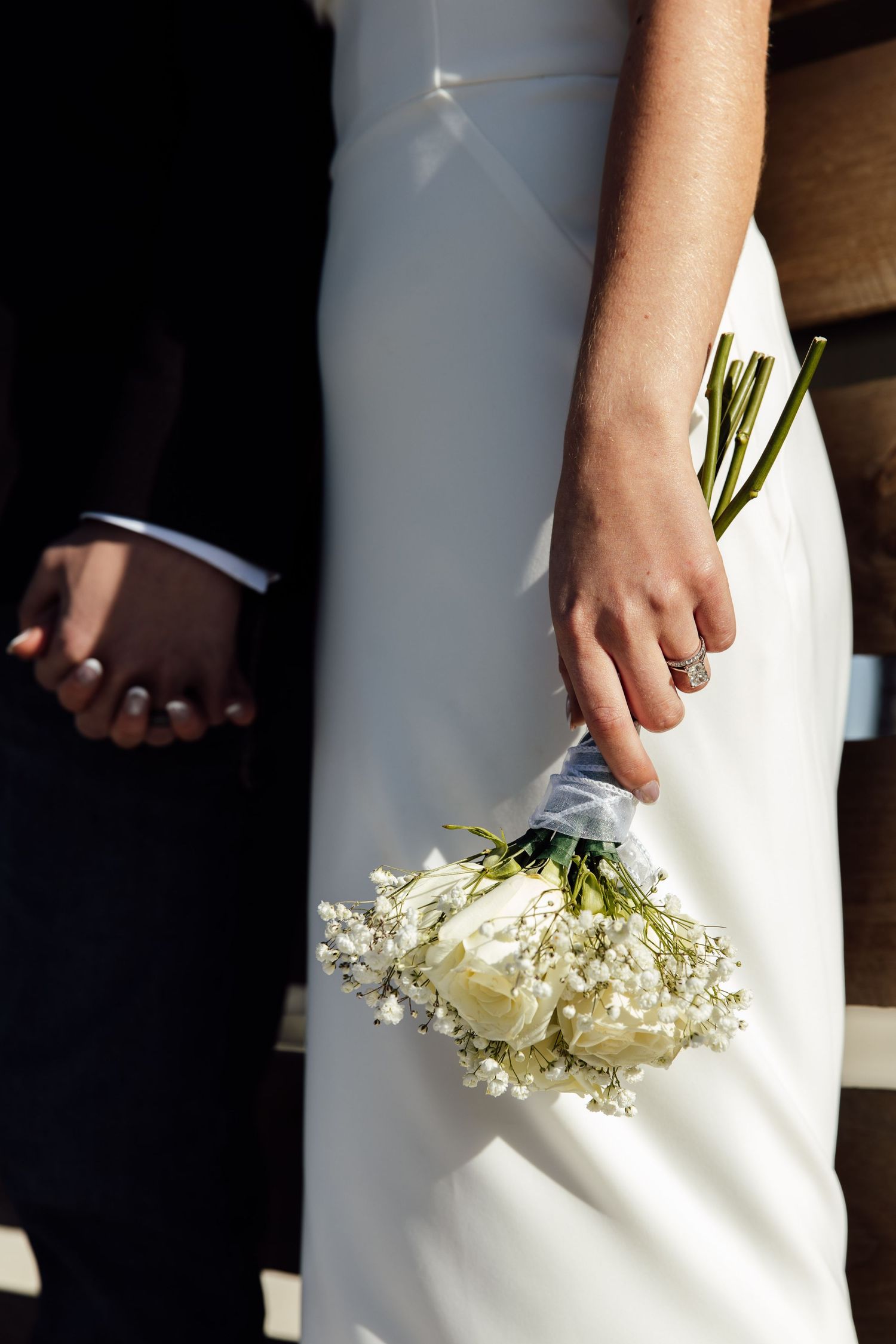Bride in white gown holding small bouquet of white roses and baby's breath, standing beside groom. Documentary wichita wedding photography