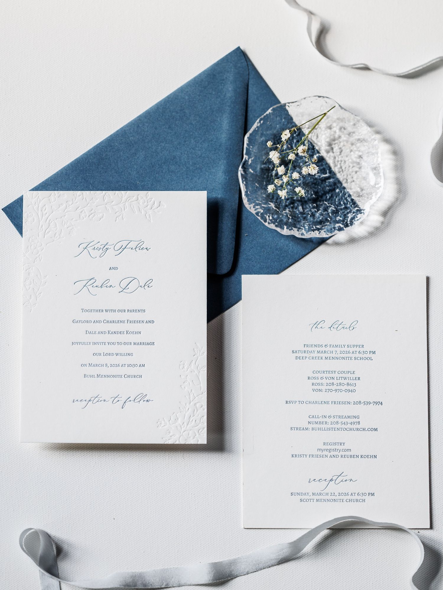 Elegant letterpress wedding invitation suite with navy blue envelope and delicate floral details on white background.