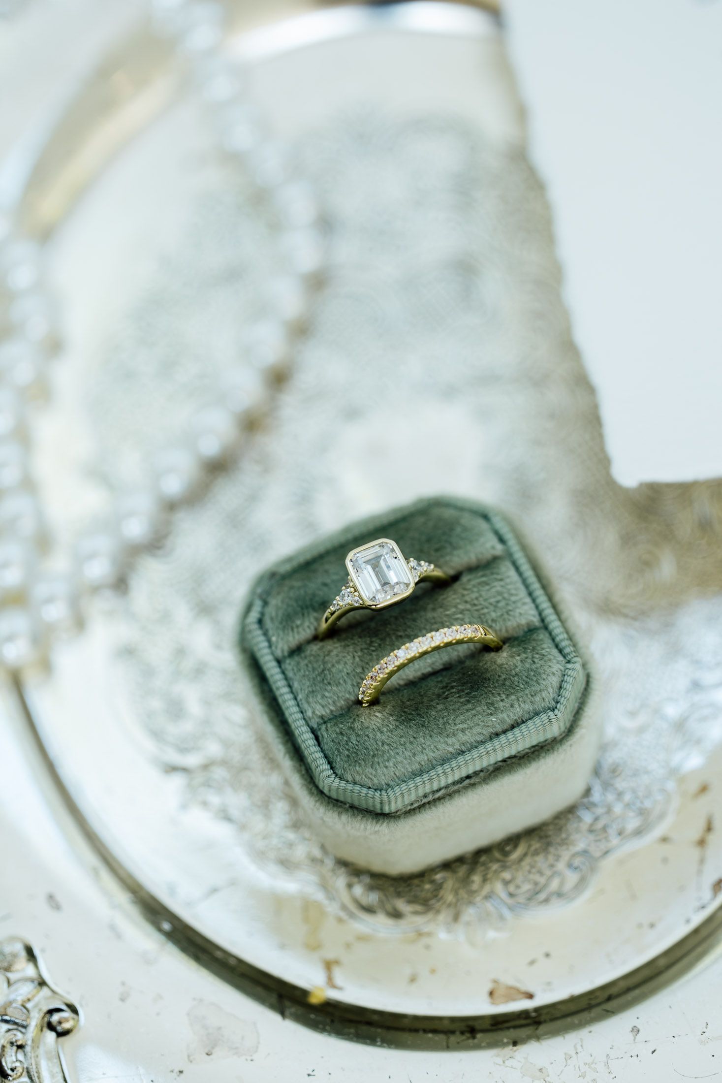 Two gold wedding rings with diamonds displayed in a green velvet ring box on a silver tray.