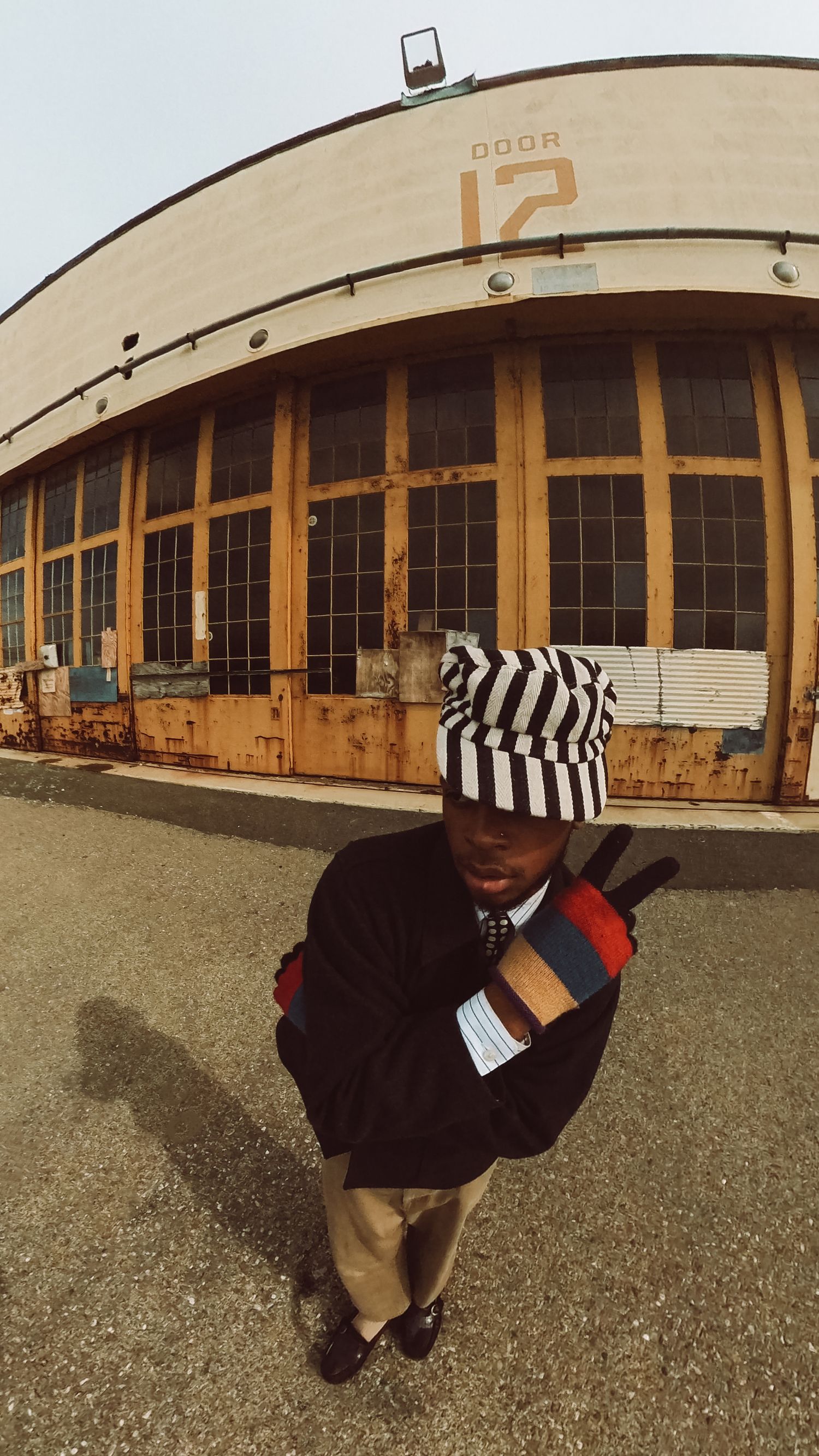 Artistic portrait of Ajai Kasim in front of a warehouse building at the Alameda Naval Base, highlighting fashion and creativity.