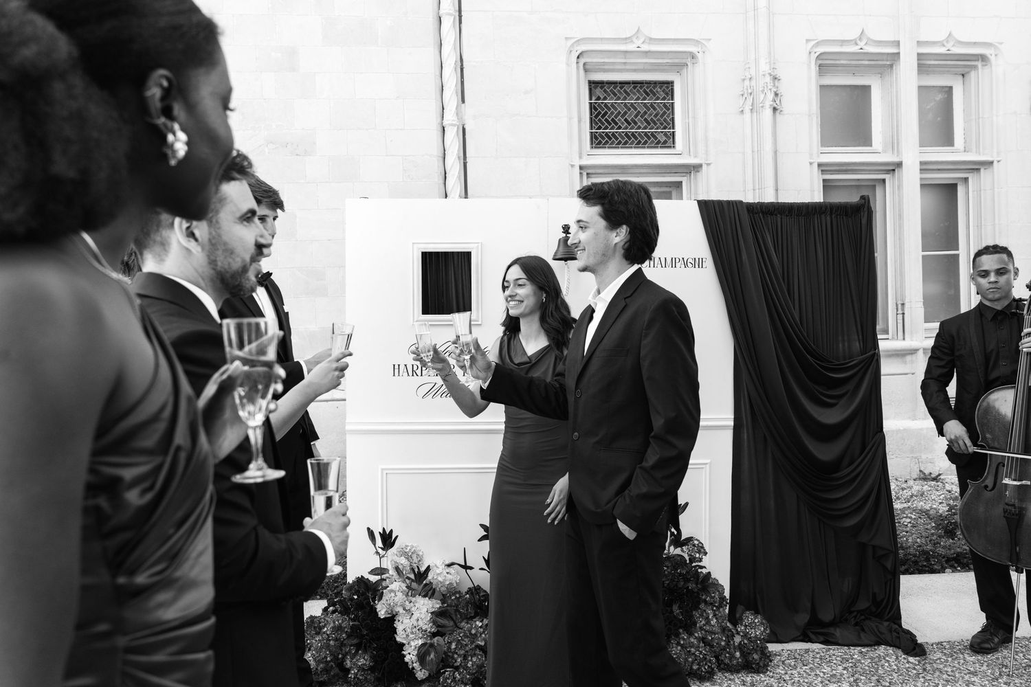 Elegant black and white photo of guests socializing at a formal outdoor evening event near a classic building.