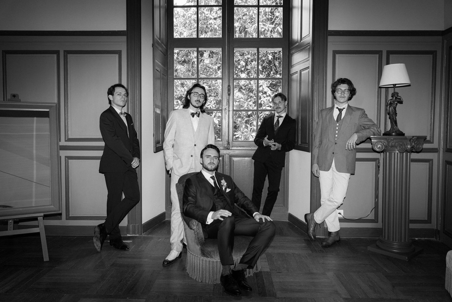 Elegant black and white photo of wedding party members in formal attire inside historic building.