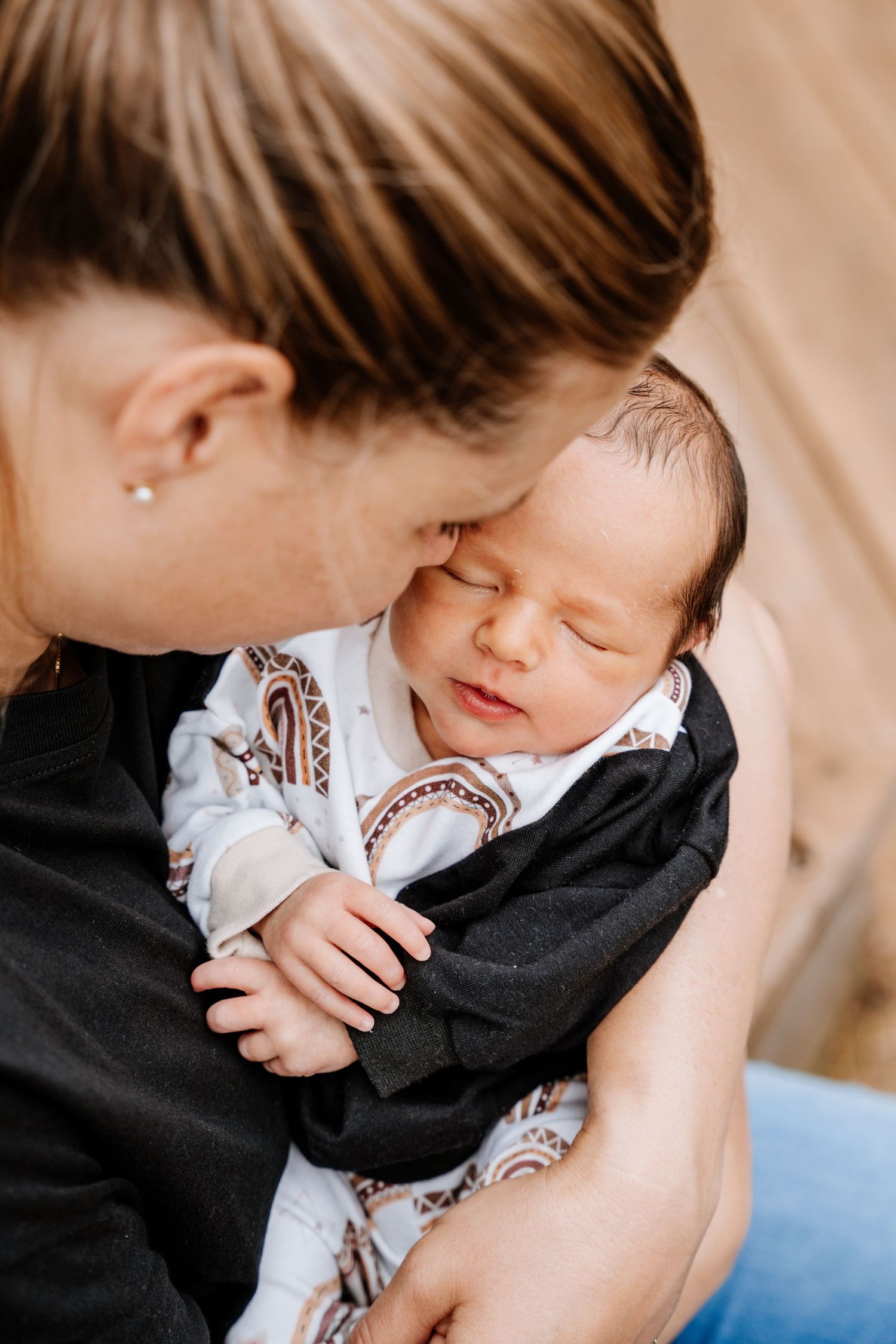 A parent in a black sweater tenderly holds and comforts their baby wearing a white onesie.