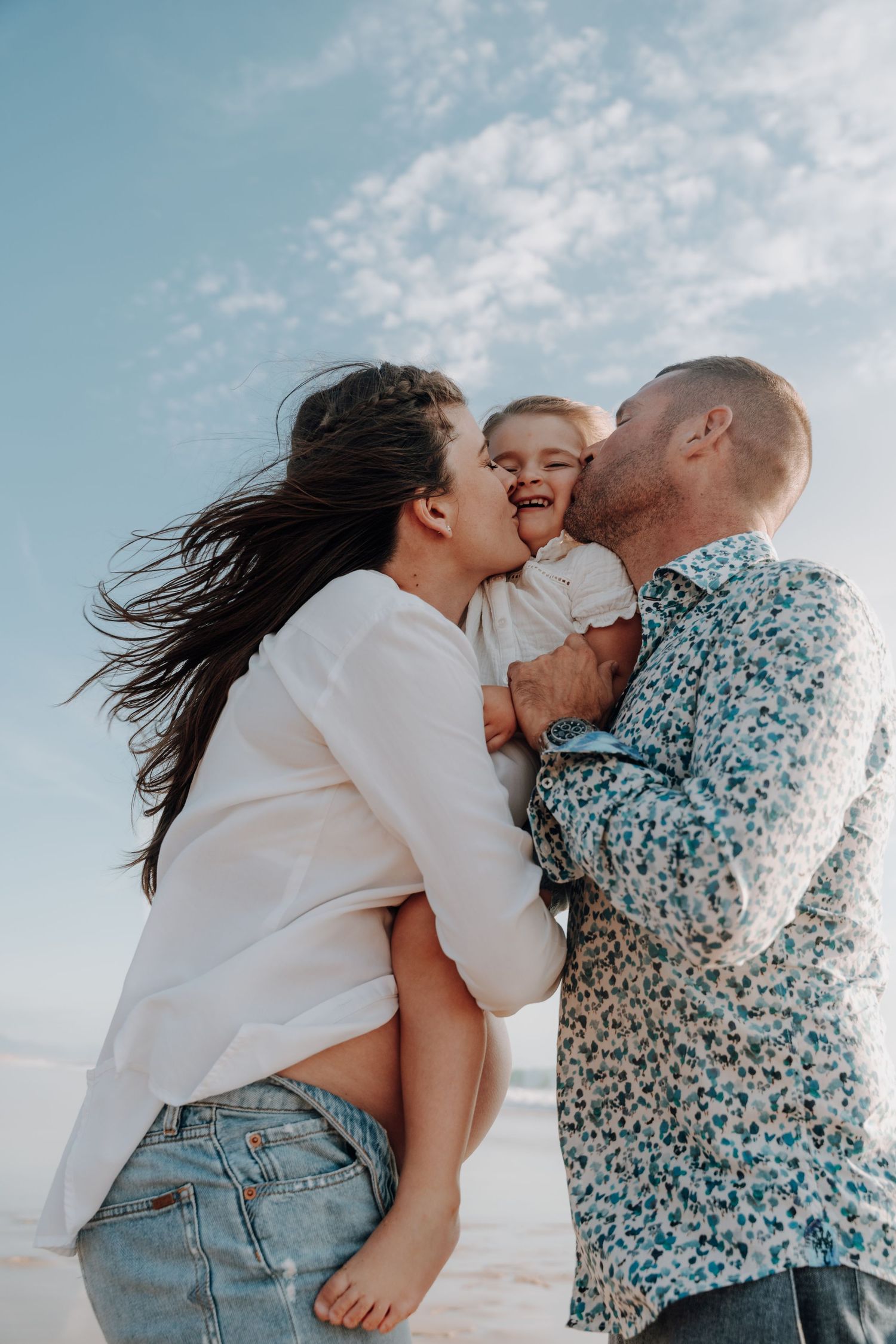 Family sharing intimate moment together on beach with blue sky backdrop.