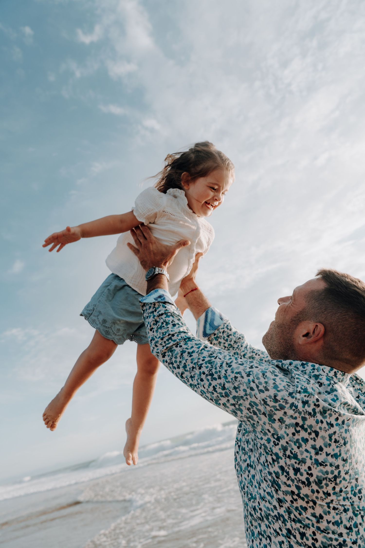 Playful moment of a child being lifted into the air against a blue sky.
