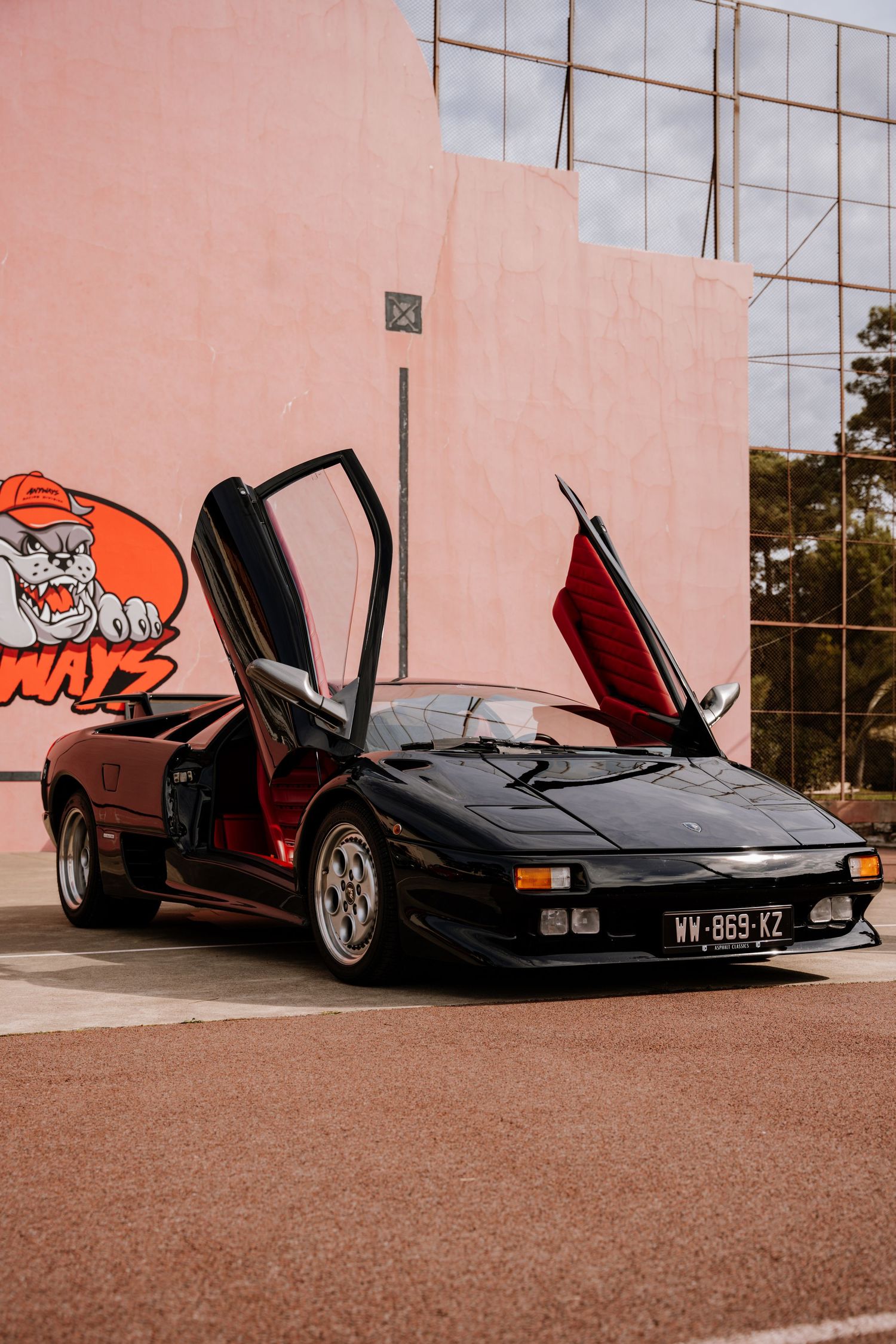 A black vintage Lamborghini Countach with scissor doors open parked against a pink wall in multiple angles.