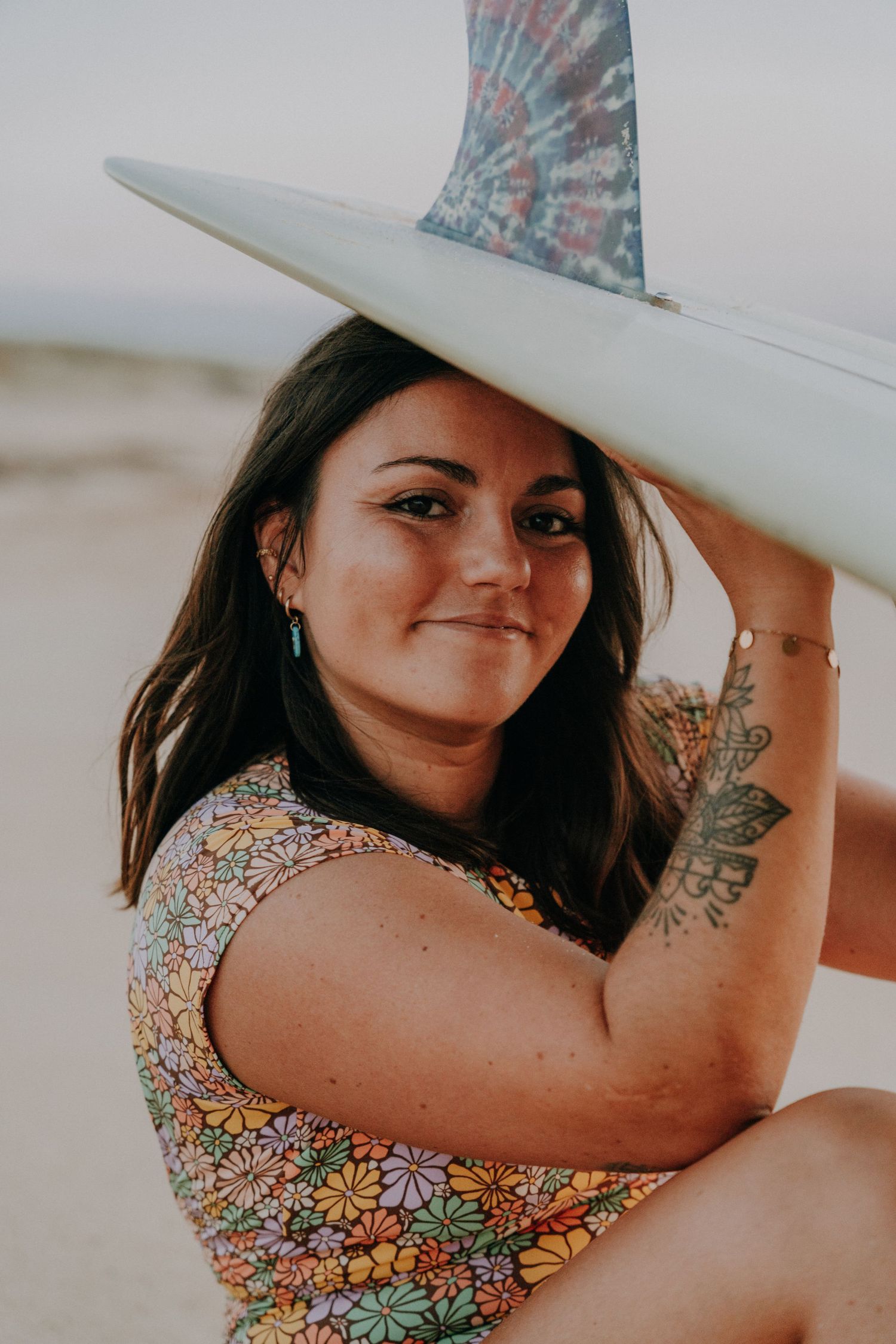 Beach photoshoot featuring someone holding a surfboard in a floral print swimsuit.