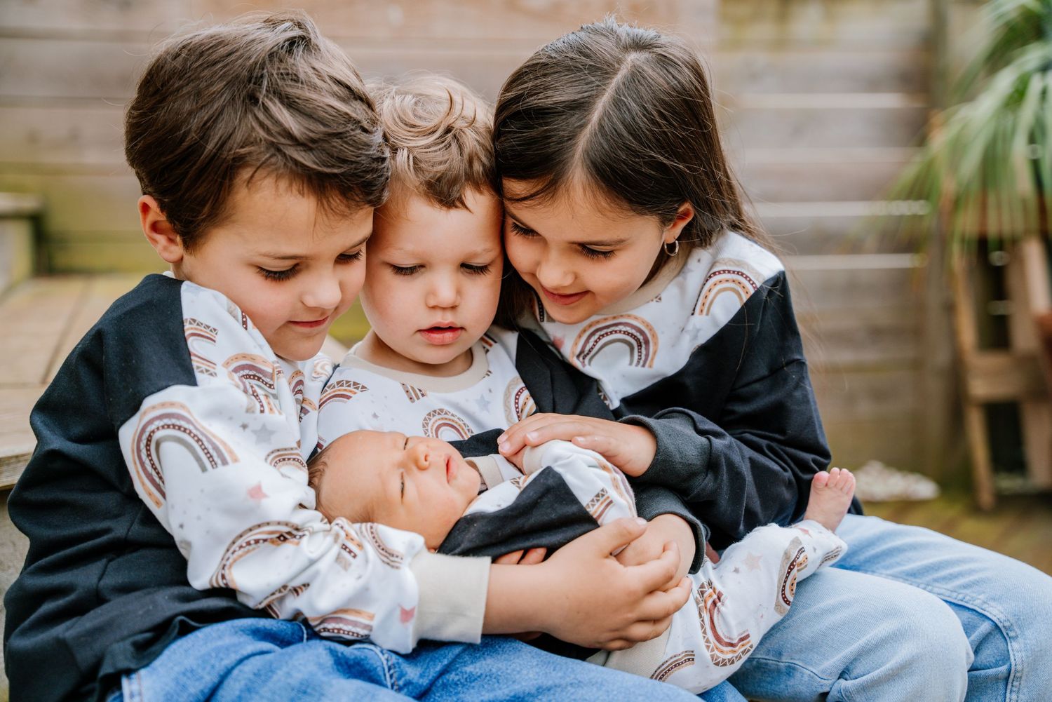 Three children in coordinated outfits sit close together on stone steps while looking at something in their hands.