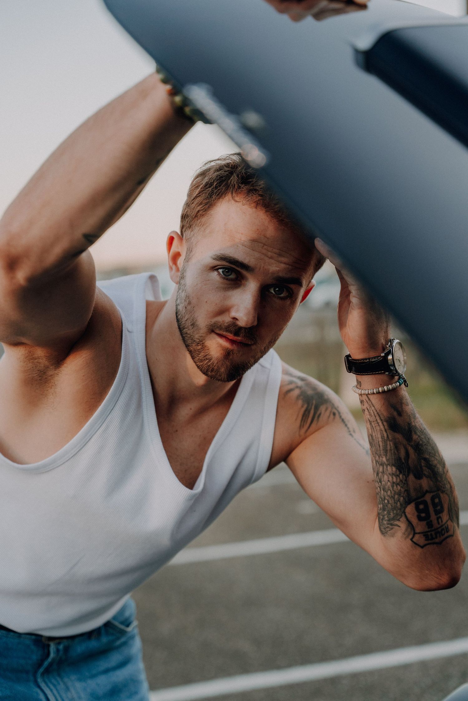Close-up shots of a person in a white tank top showing tattooed arms against a blurred background.