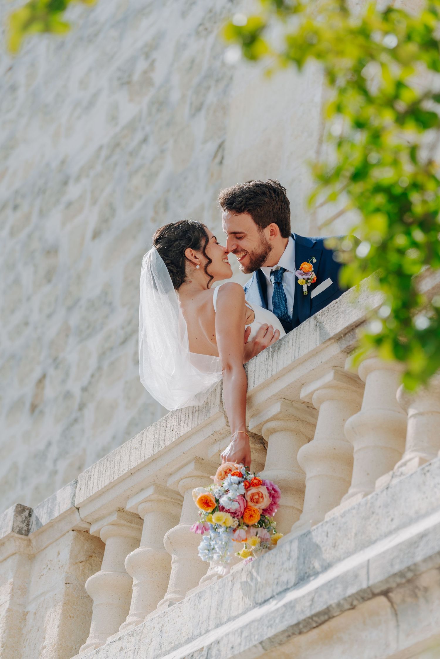 Romantic wedding portrait on stone balcony with colorful florals and greenery.